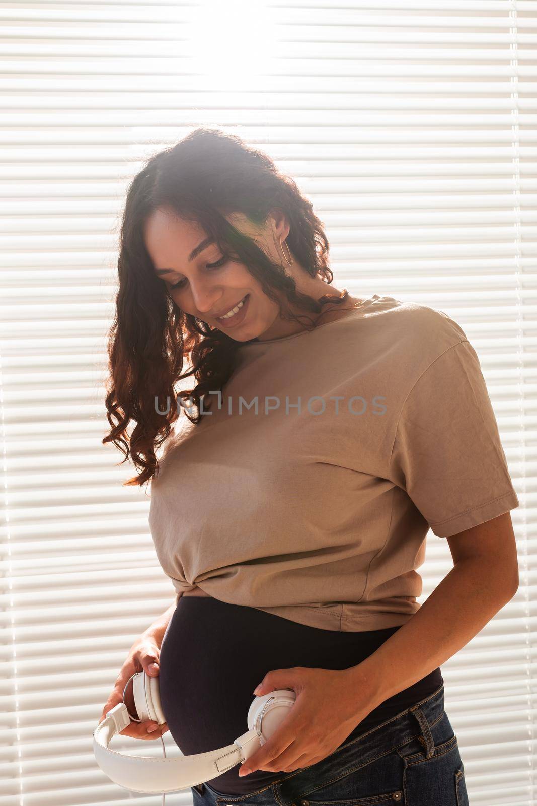 Smiling brunette pacified pregnant woman listening to pleasant music using a smartphone and headphones. Sedation therapy before meeting with baby
