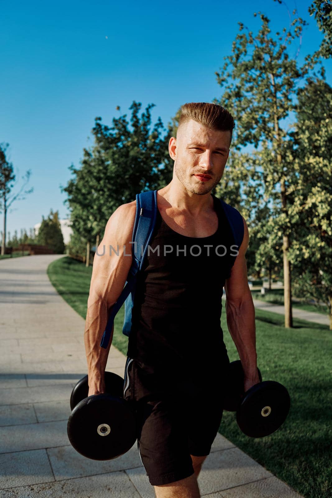 athletic man with dumbbells in his hands in the park training lifestyle by Vichizh
