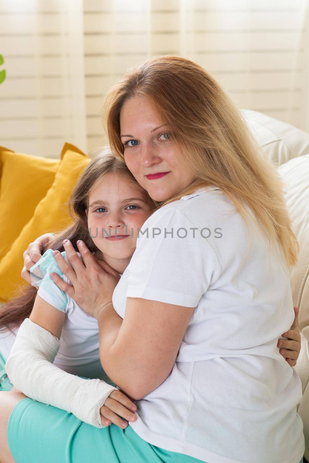 Mother hugs your child girl with a cast on a broken wrist or arm smiling. Childhood illnesses, a positive outlook and recovery