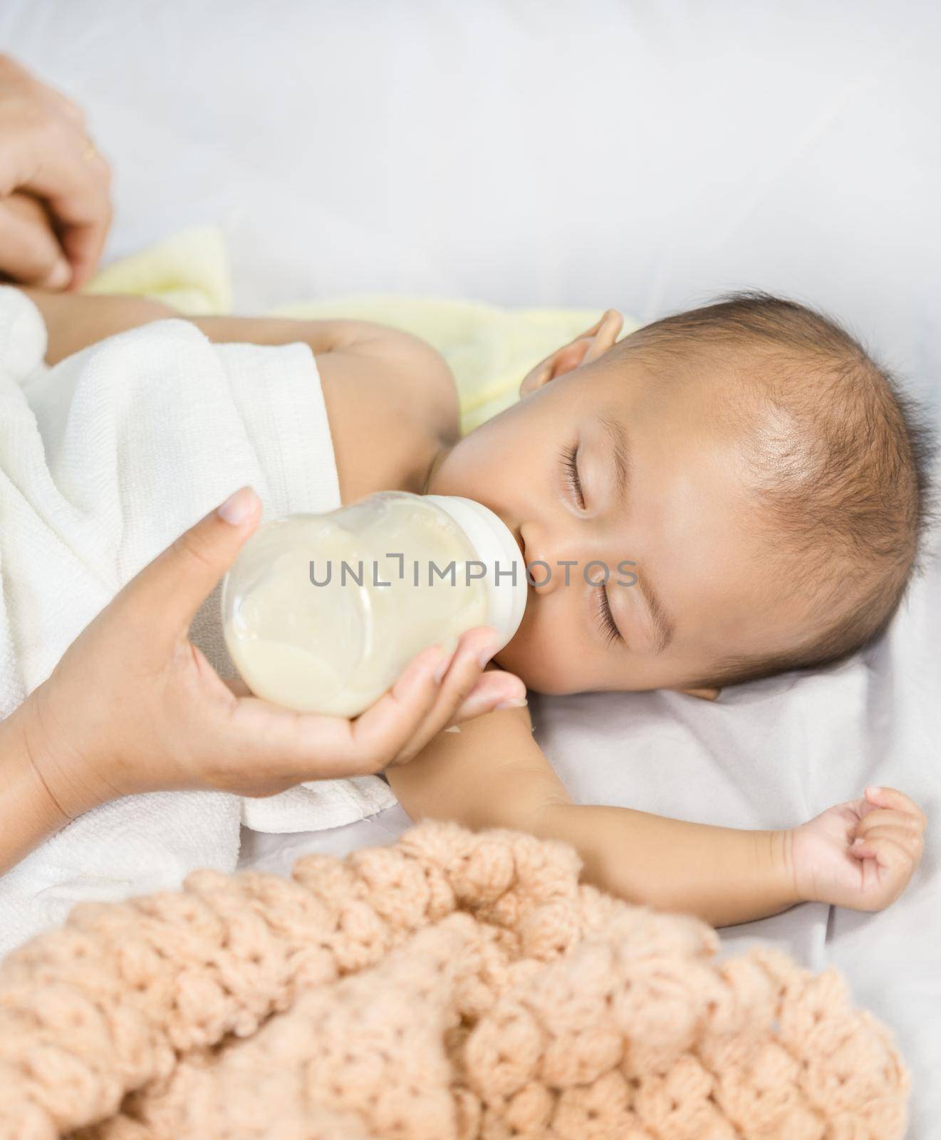 hand of mother feeding milk from bottle and baby sleeping on bed.