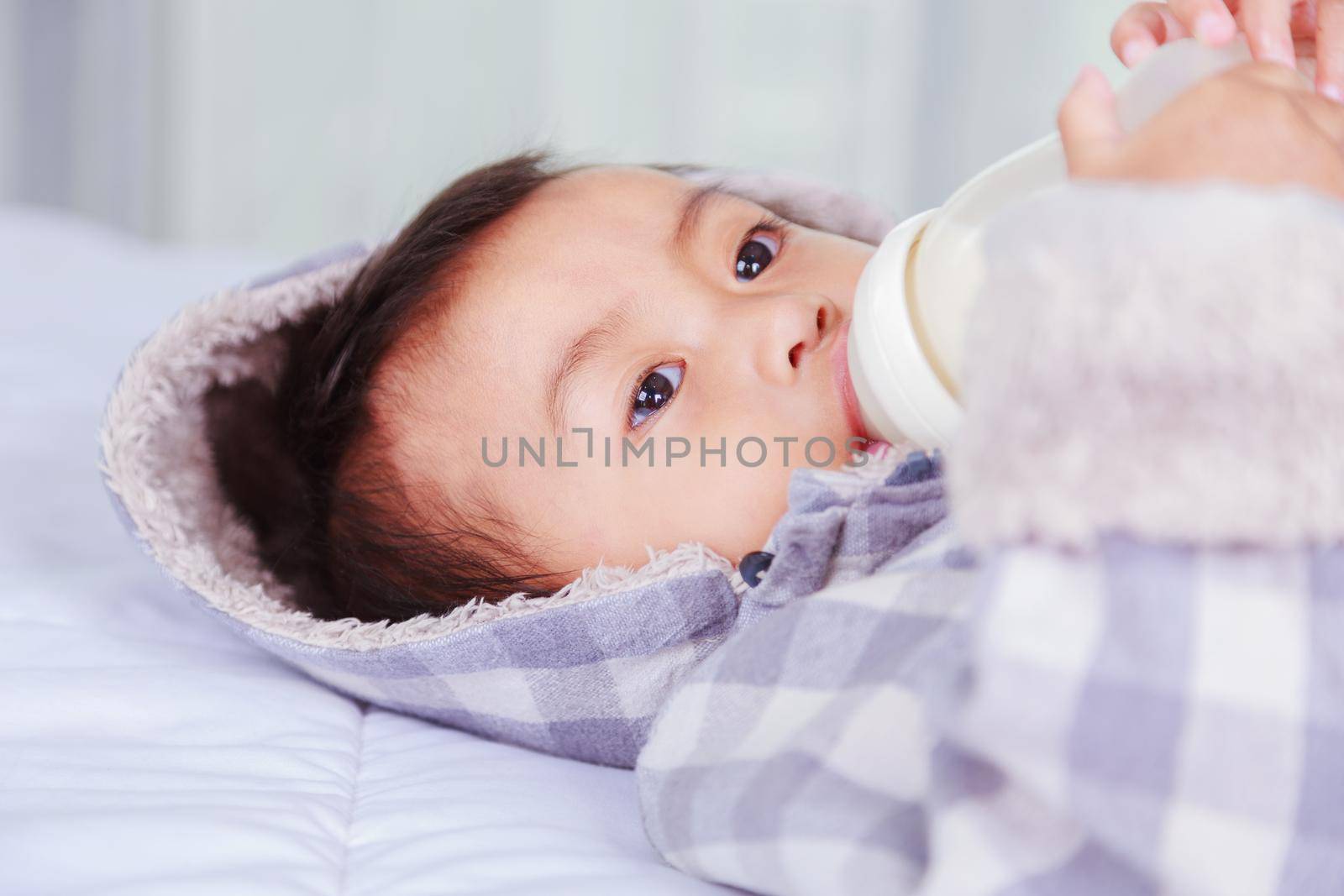 baby drinking milk with bottle on bed at home