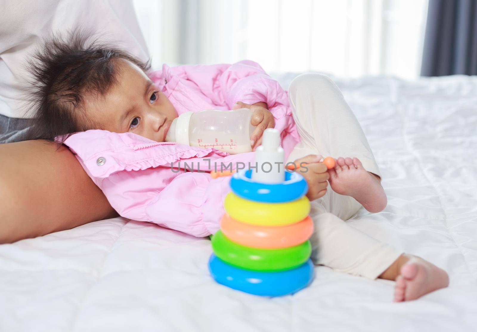 baby drinking a milk from bottle with mother on a bed