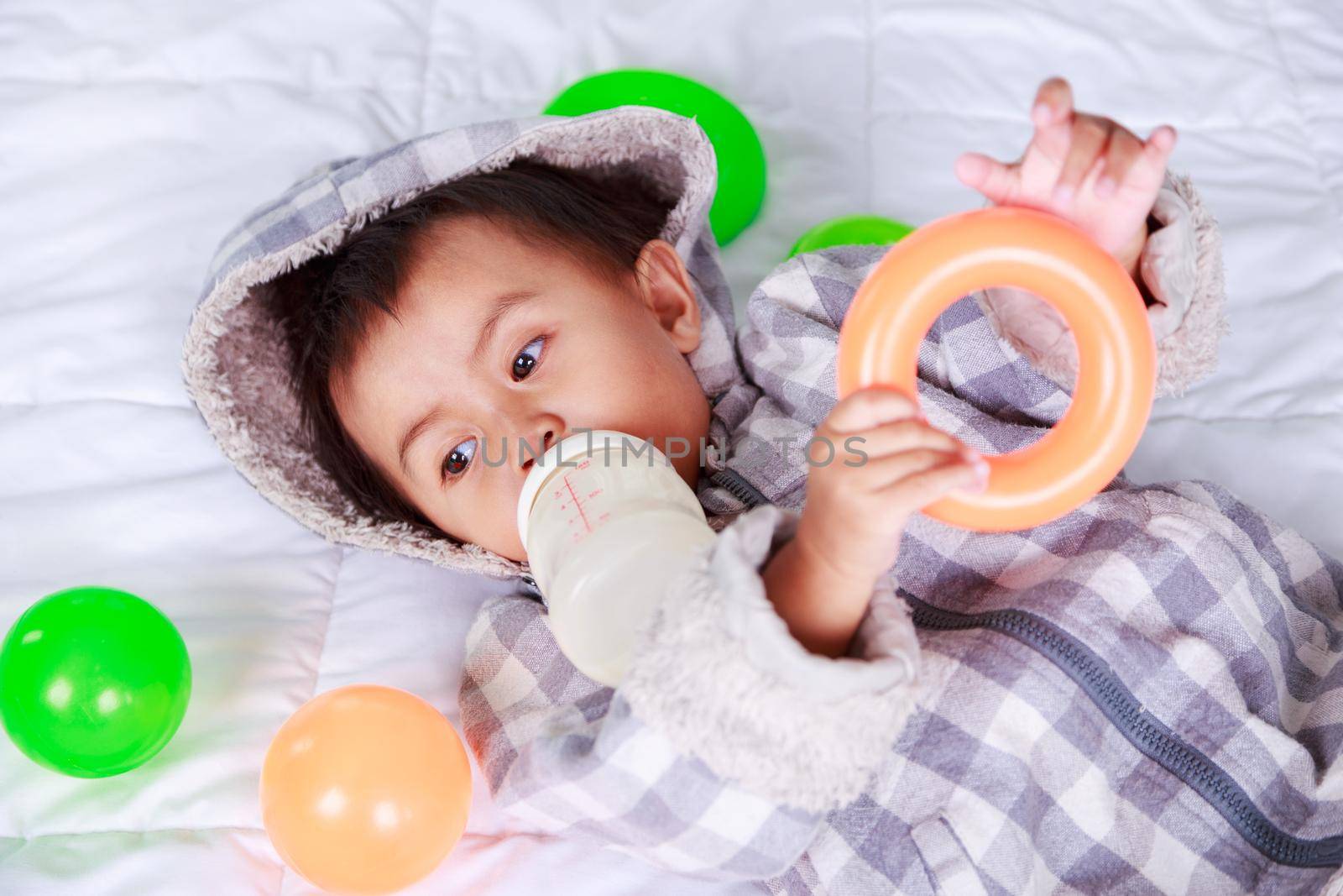 baby drinking milk with bottle on bed at home