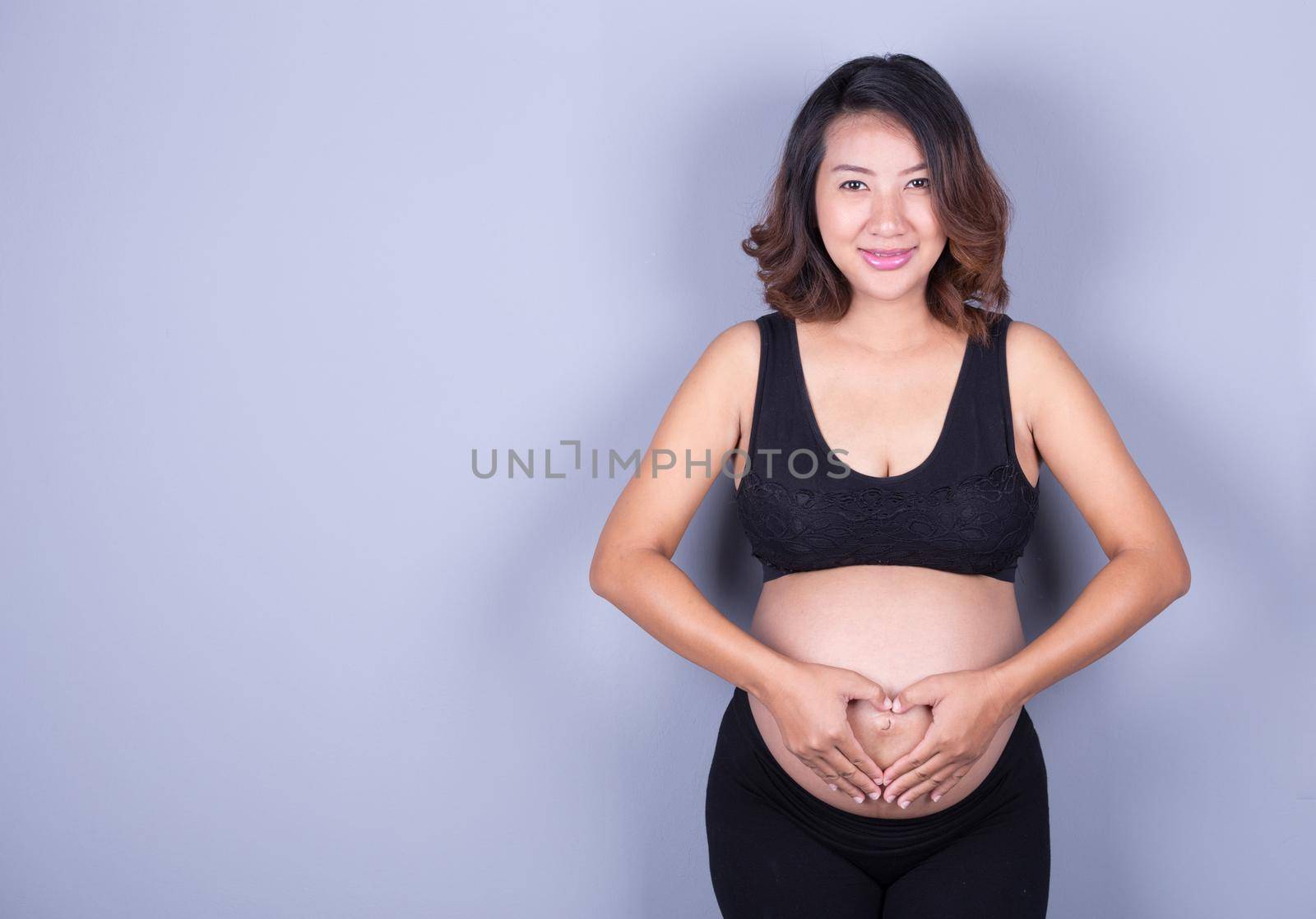 Pregnant Woman holding her hands in a heart shape on belly by geargodz