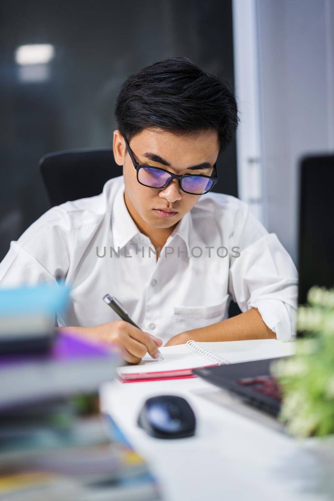 young man studying and writing on notebook with laptop  by geargodz