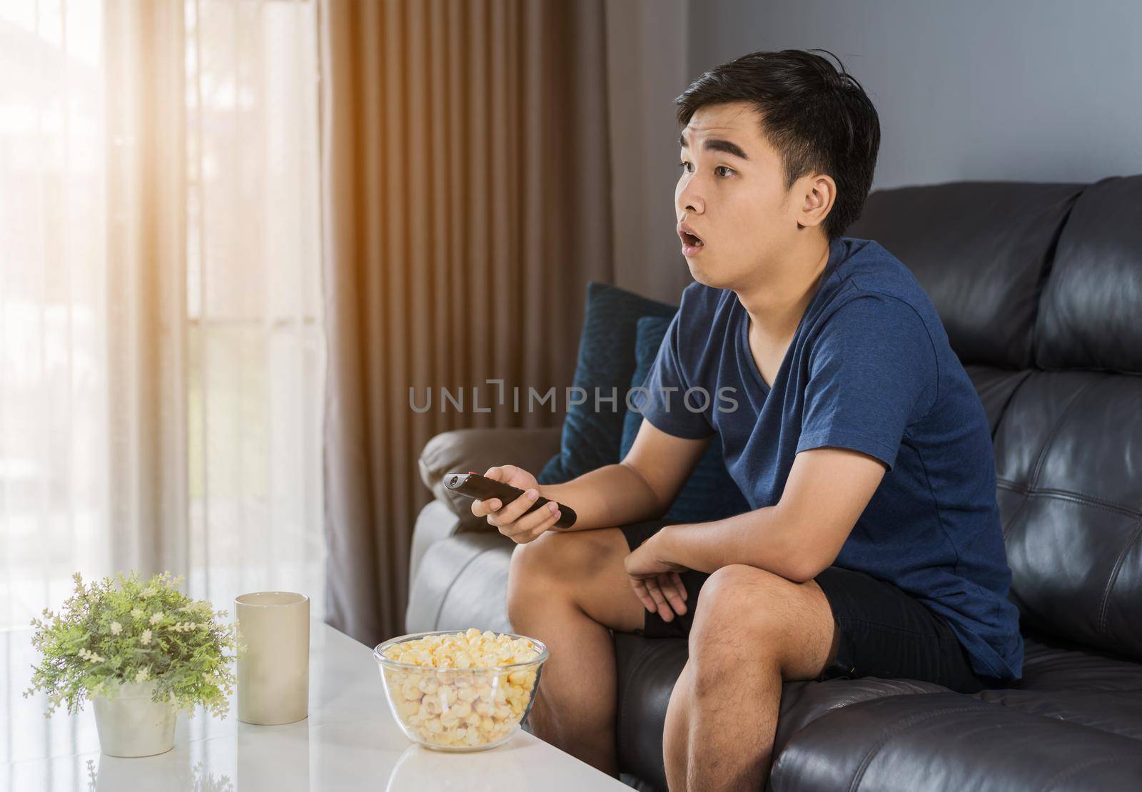 Shocked young man watching at tv and sitting on sofa in the living room