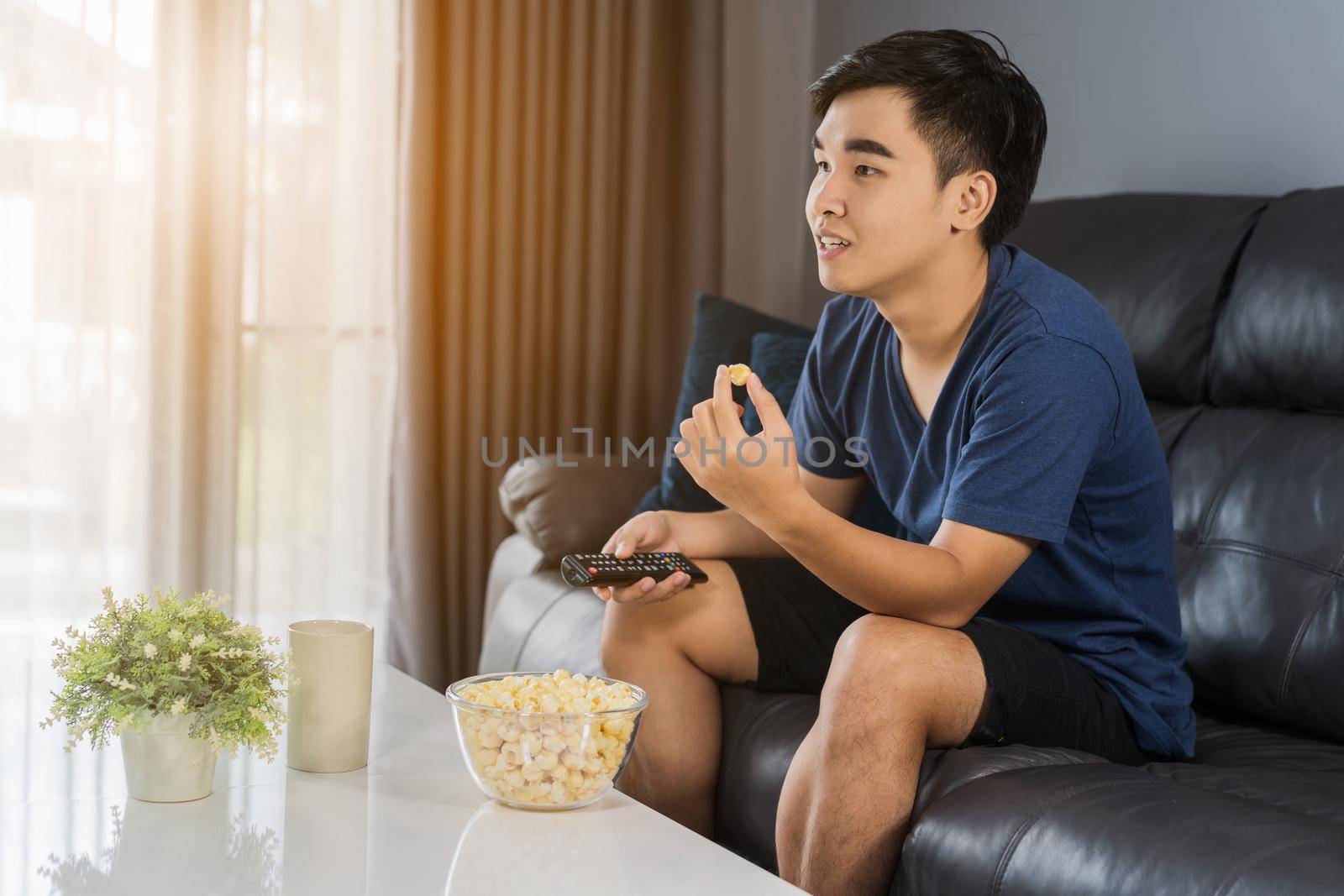 young man eating popcorn while sitting on a couch at home and watching TV