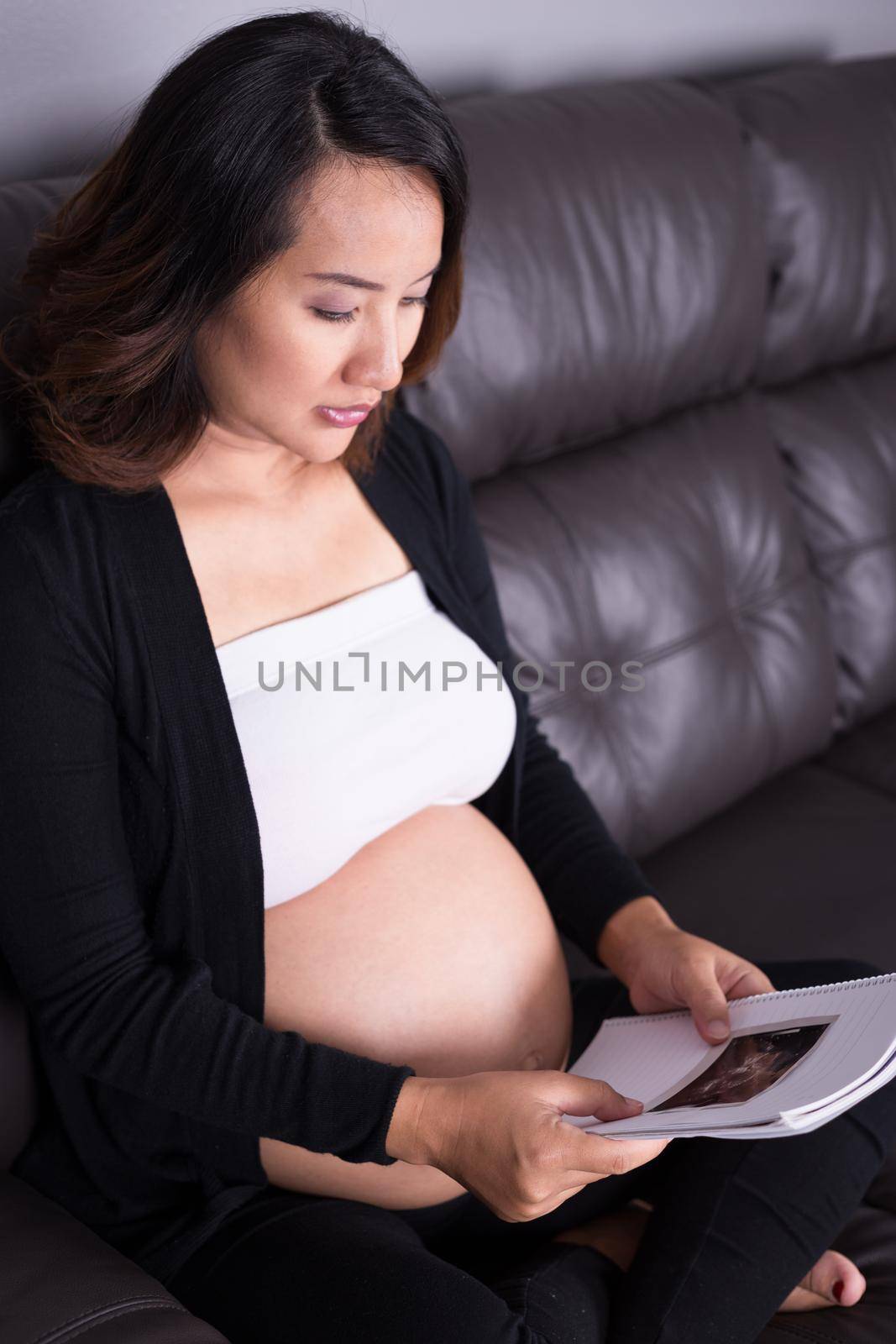 Pregnant woman sitting on sofa and holding her child ultrasound picture