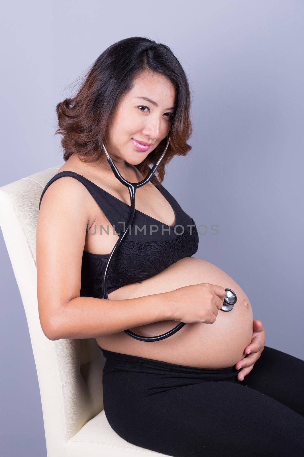 pretty young pregnant asian woman with stethoscope listening belly to baby