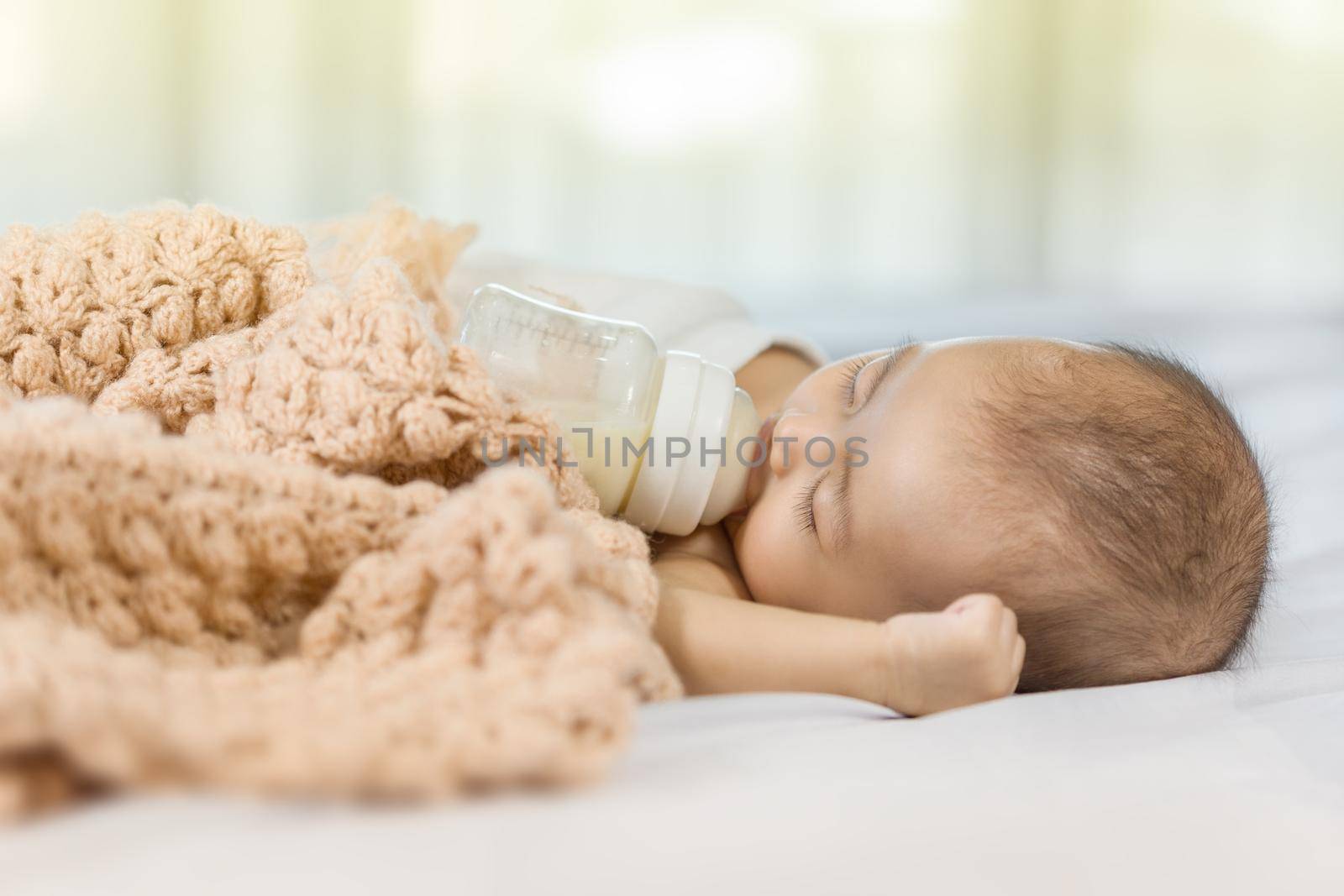 baby drinking milk from bottle and sleeping on bed at home