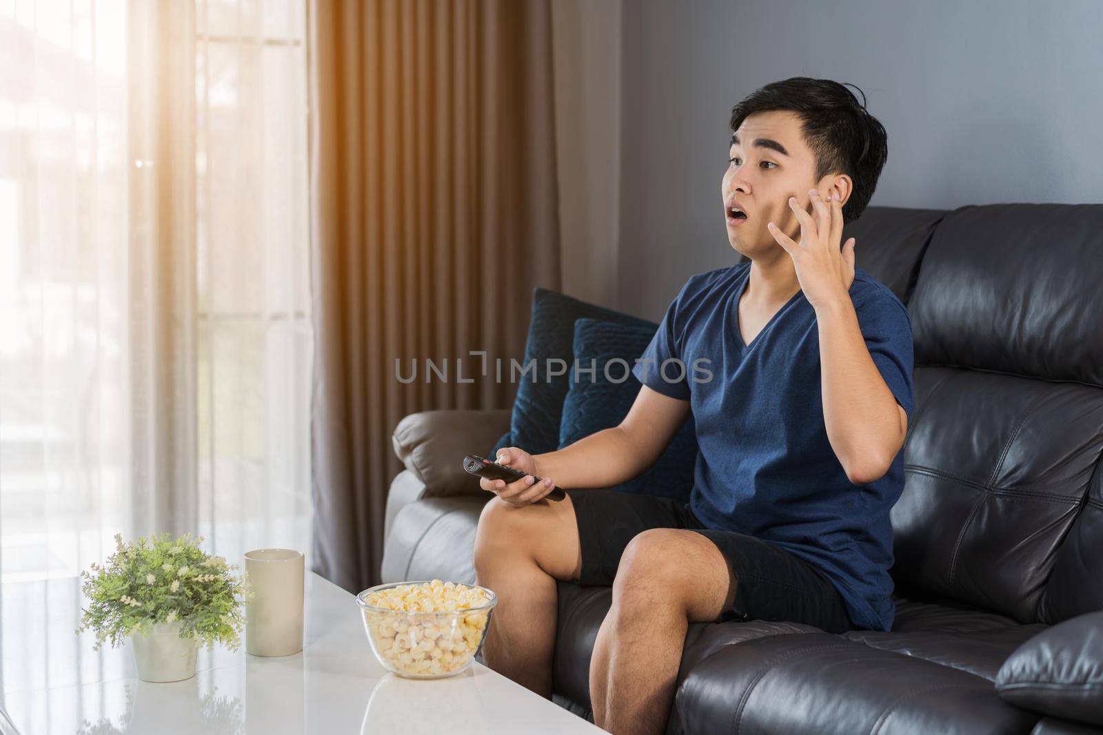 Shocked young man watching at tv and sitting on sofa in the living room