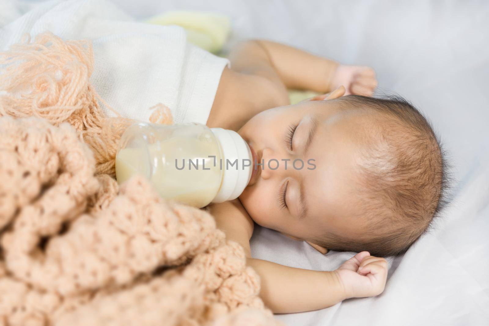 baby drinking milk from bottle and sleeping on bed at home