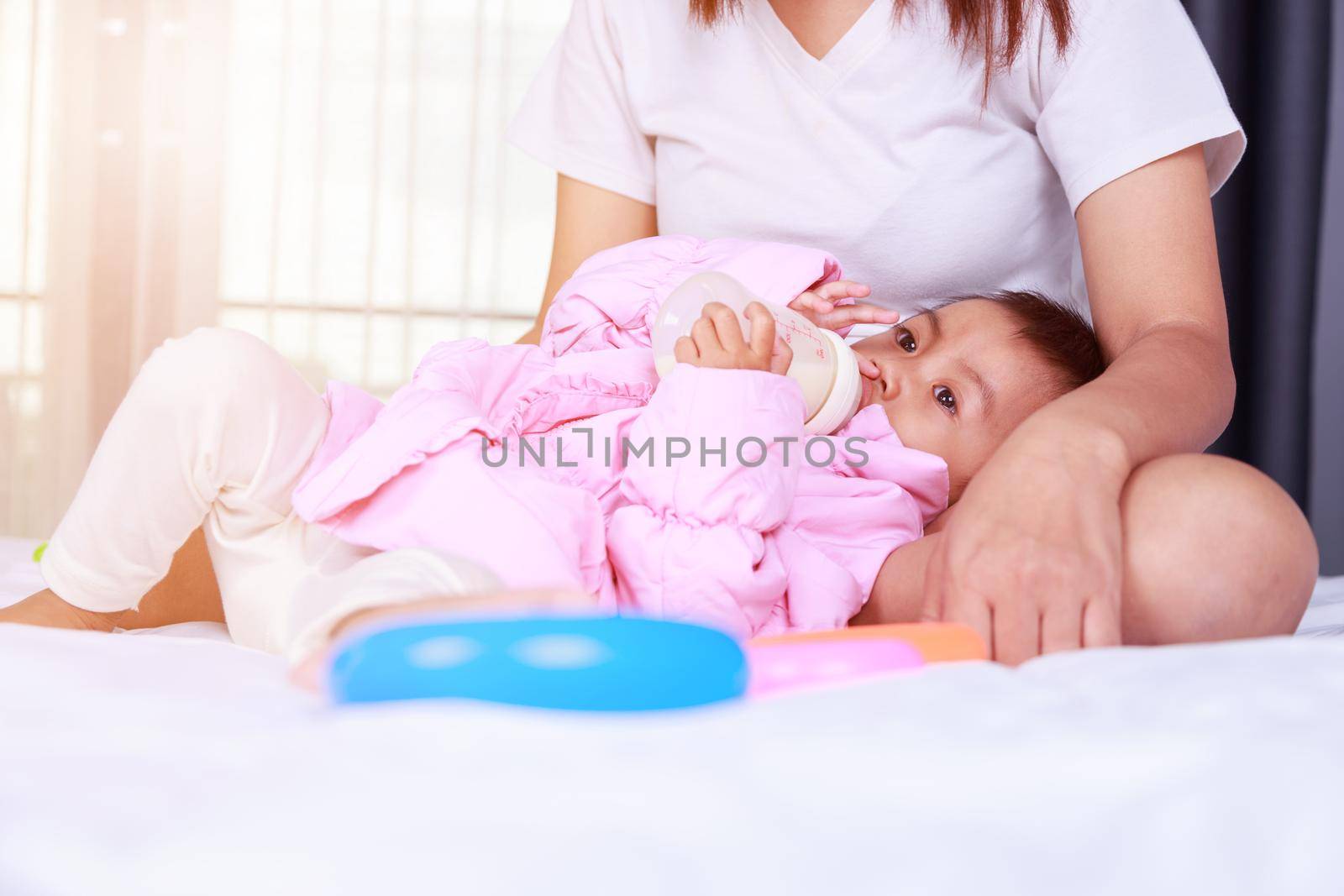 baby drinking a milk from bottle with mother on a bed