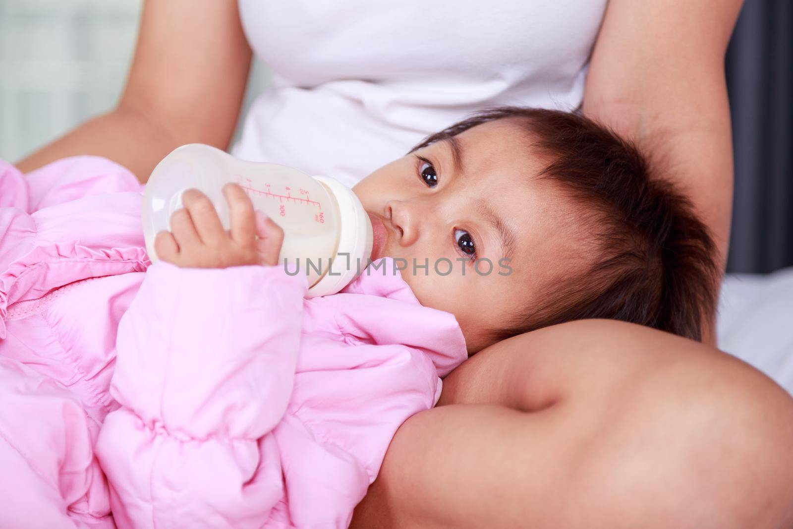 baby drinking a milk from bottle with mother on bed by geargodz