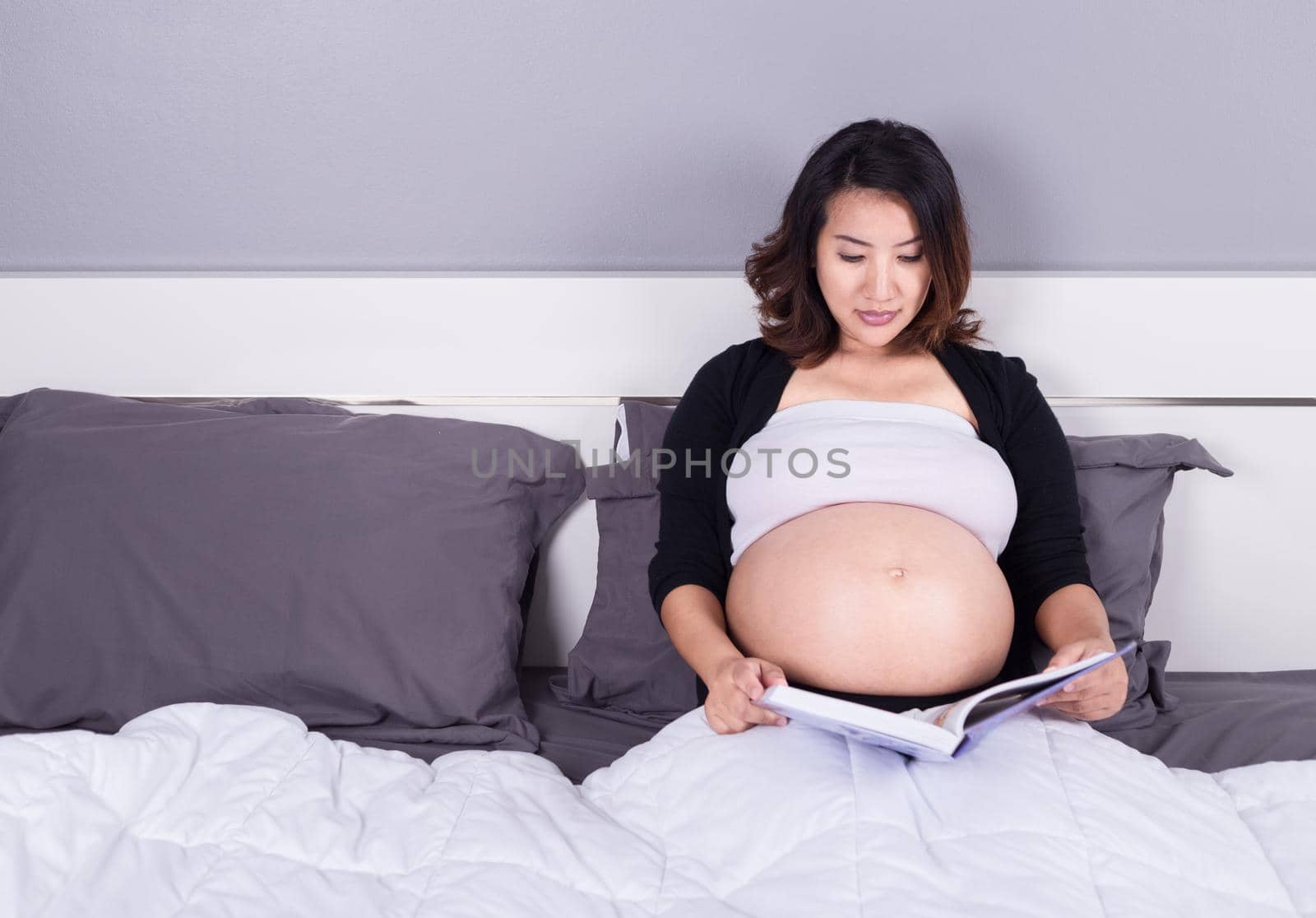 pregnant woman reading a book while lying on a bed in the bedroom by geargodz