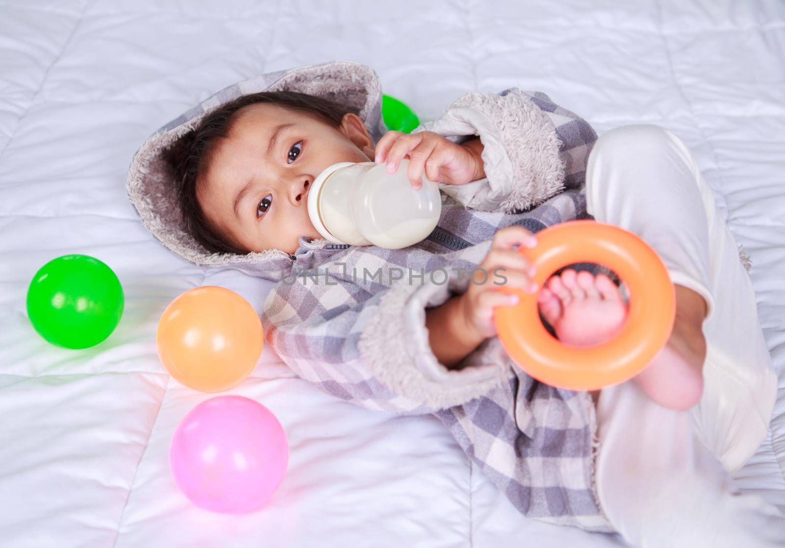 baby drinking milk with bottle on bed at home