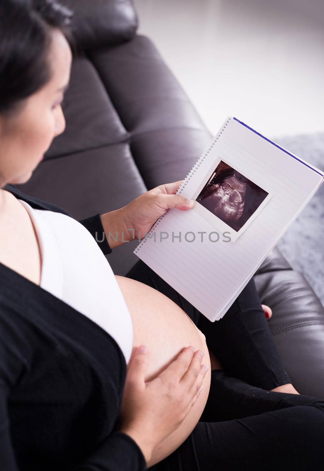 Pregnant woman sitting on sofa, holding her child ultrasound picture by geargodz