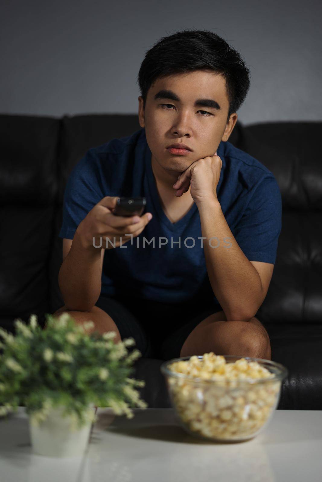 young bored man watching tv and sitting on sofa in the living room at night