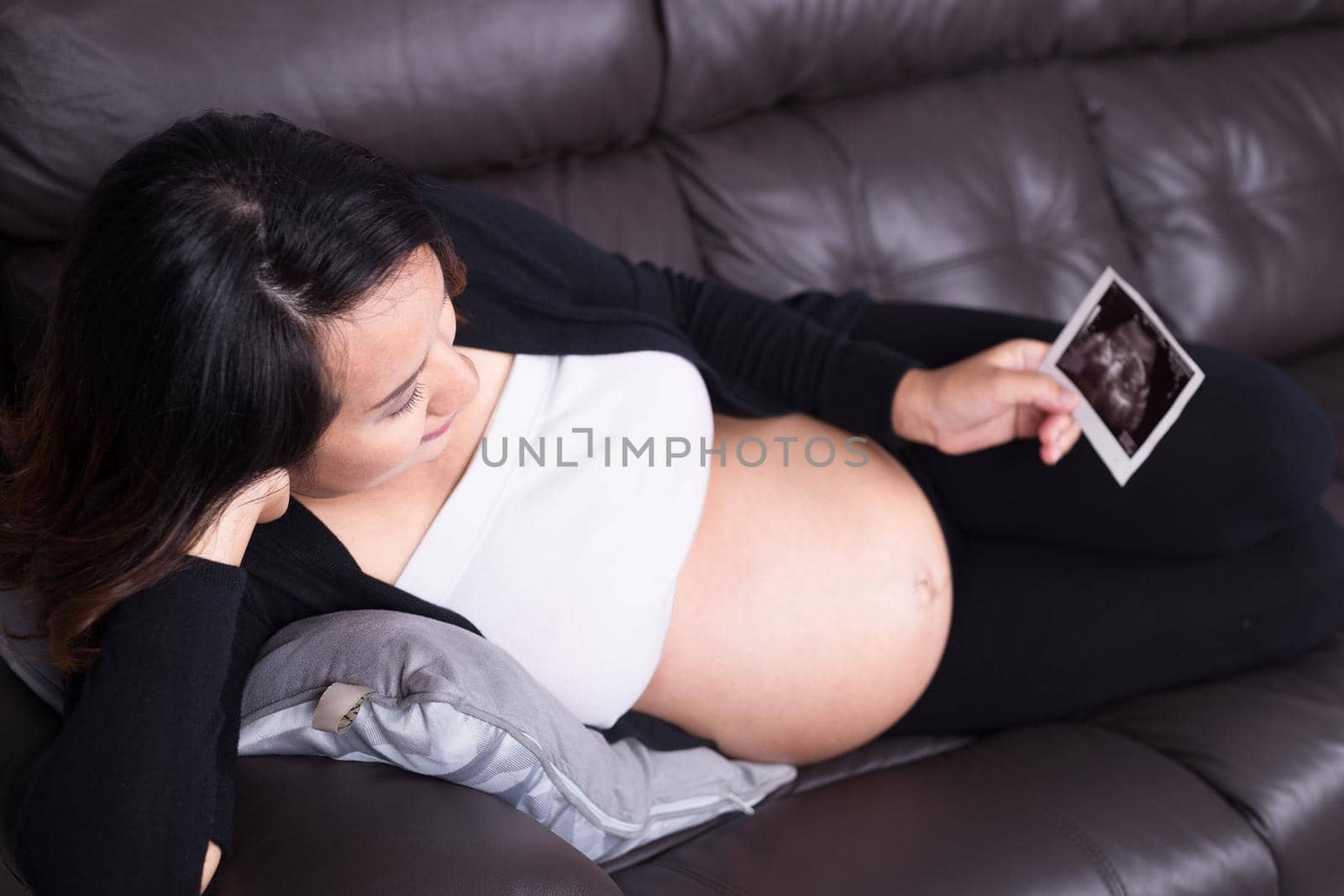 Pregnant woman resting on sofa and holding her child ultrasound picture