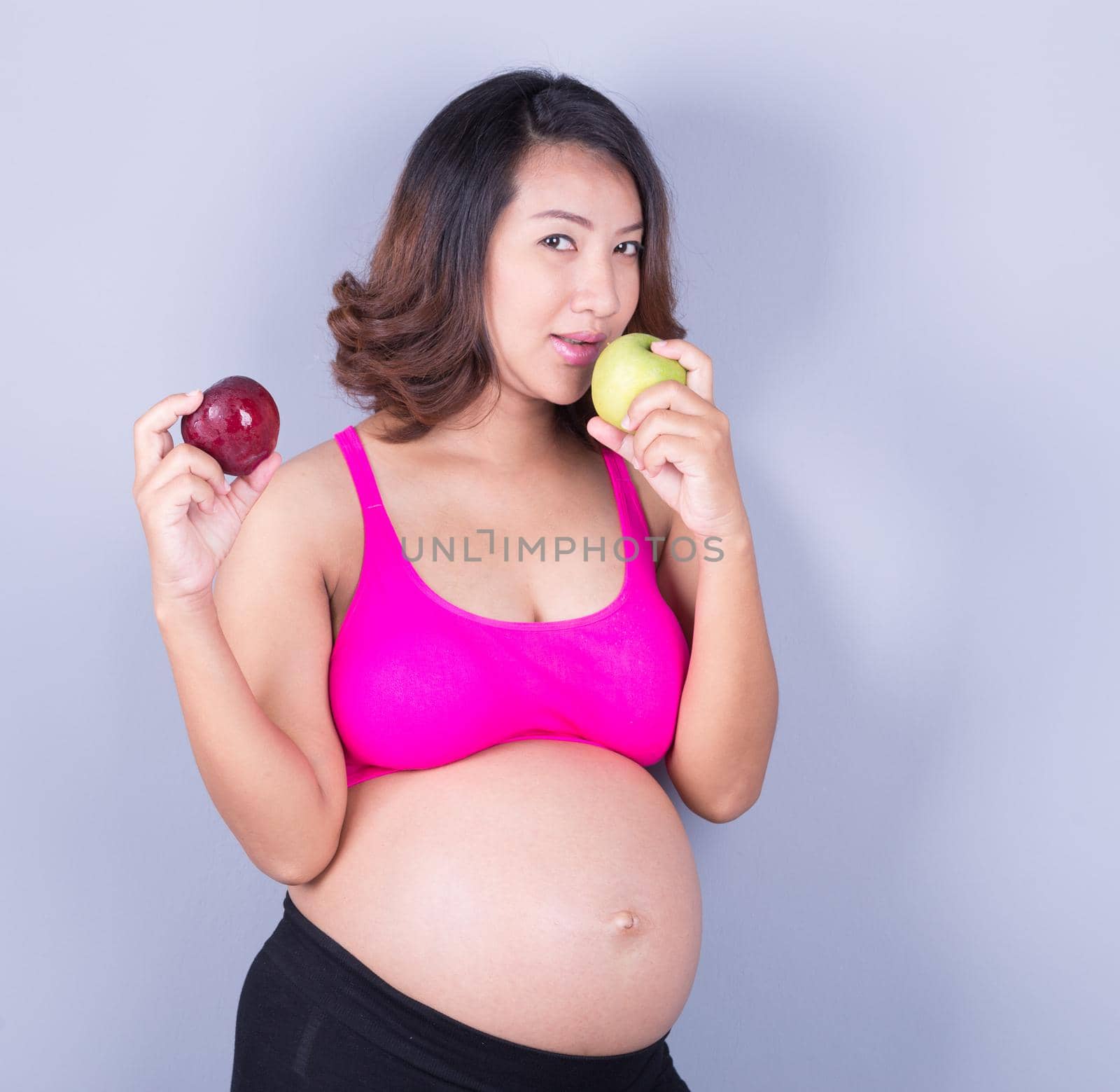 Beautiful pregnant woman with red and green apple on gray background