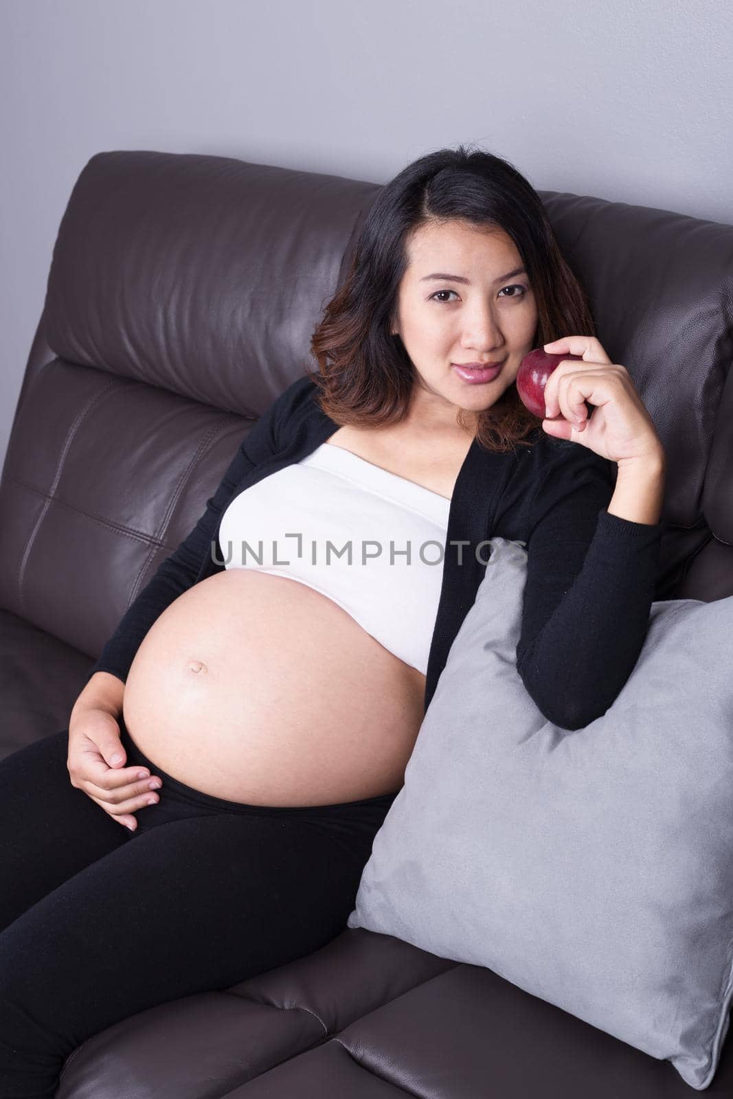 pregnant woman resting with red apple at home on sofa by geargodz