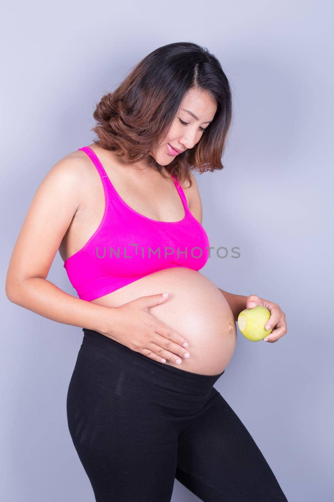 Beautiful pregnant woman with green apple on gray background