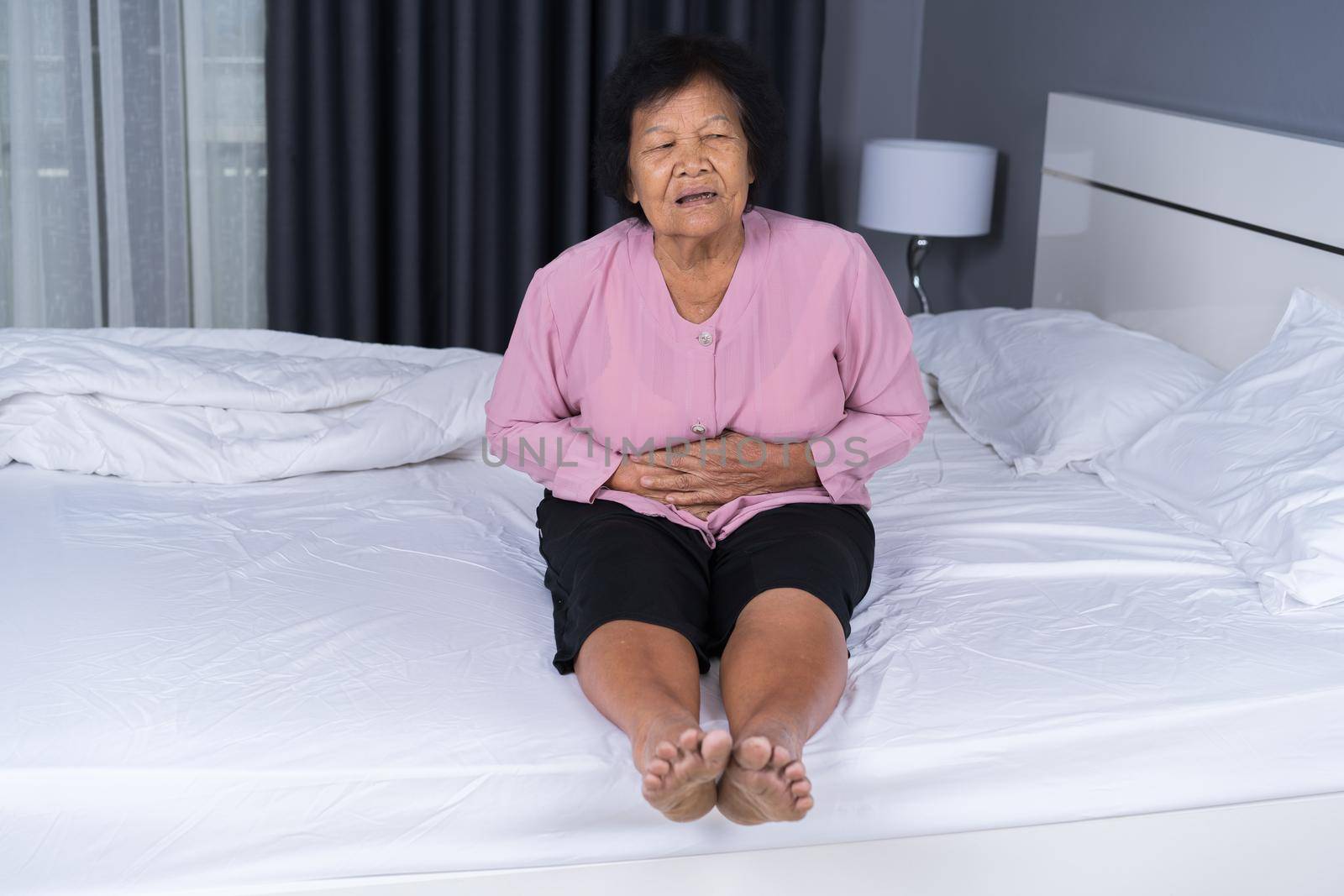 senior woman suffering from stomachache on bed at home