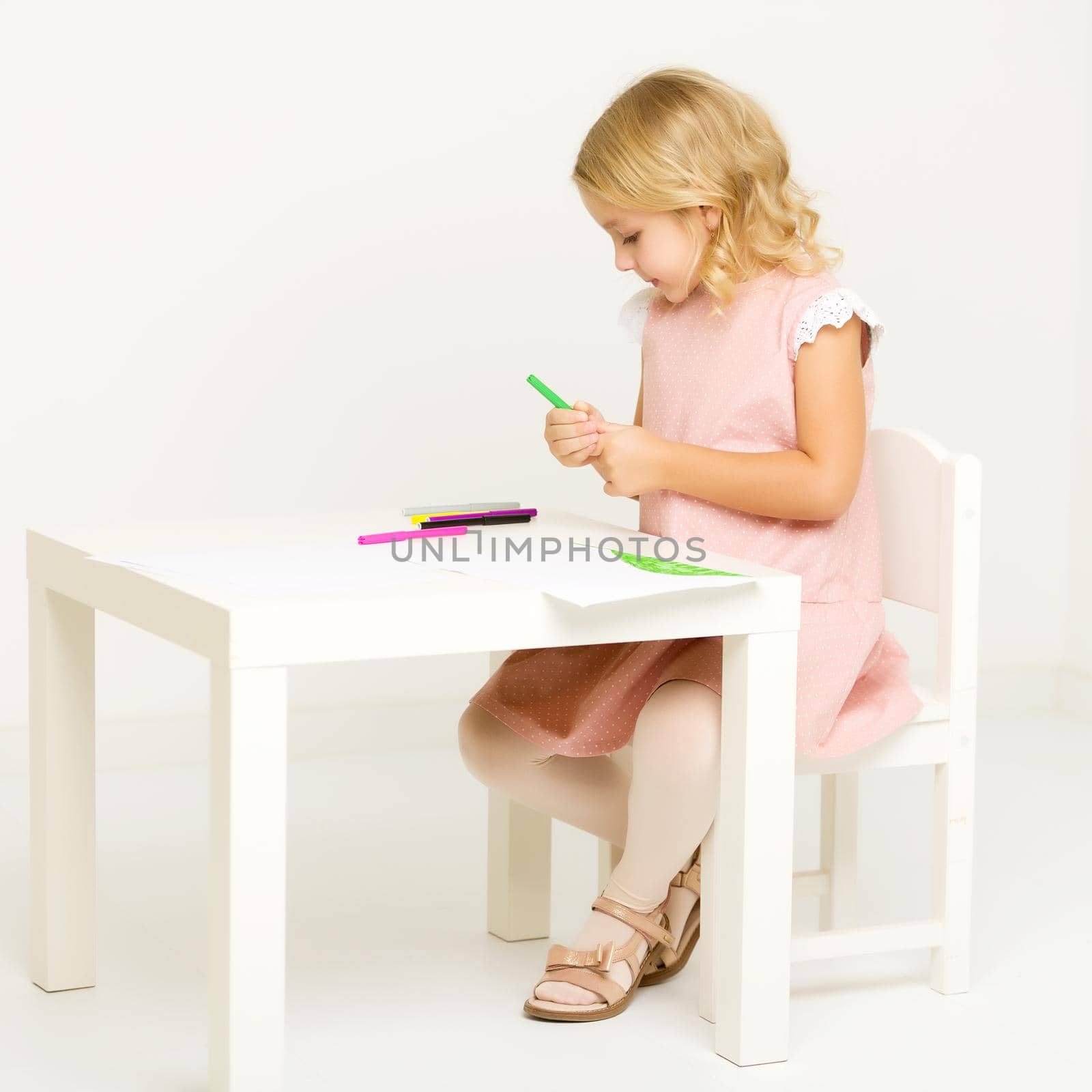 A little girl draws at a table on a piece of paper. The concept of a happy childhood, creativity, learning in school and family. Isolated on white background.