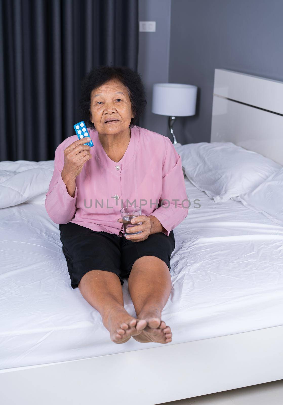senior woman taking pill with glass of water in a bed