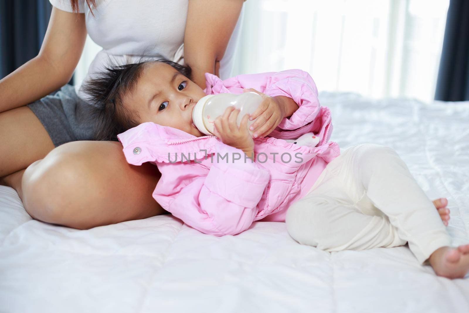 baby drinking a milk from bottle with mother on a bed