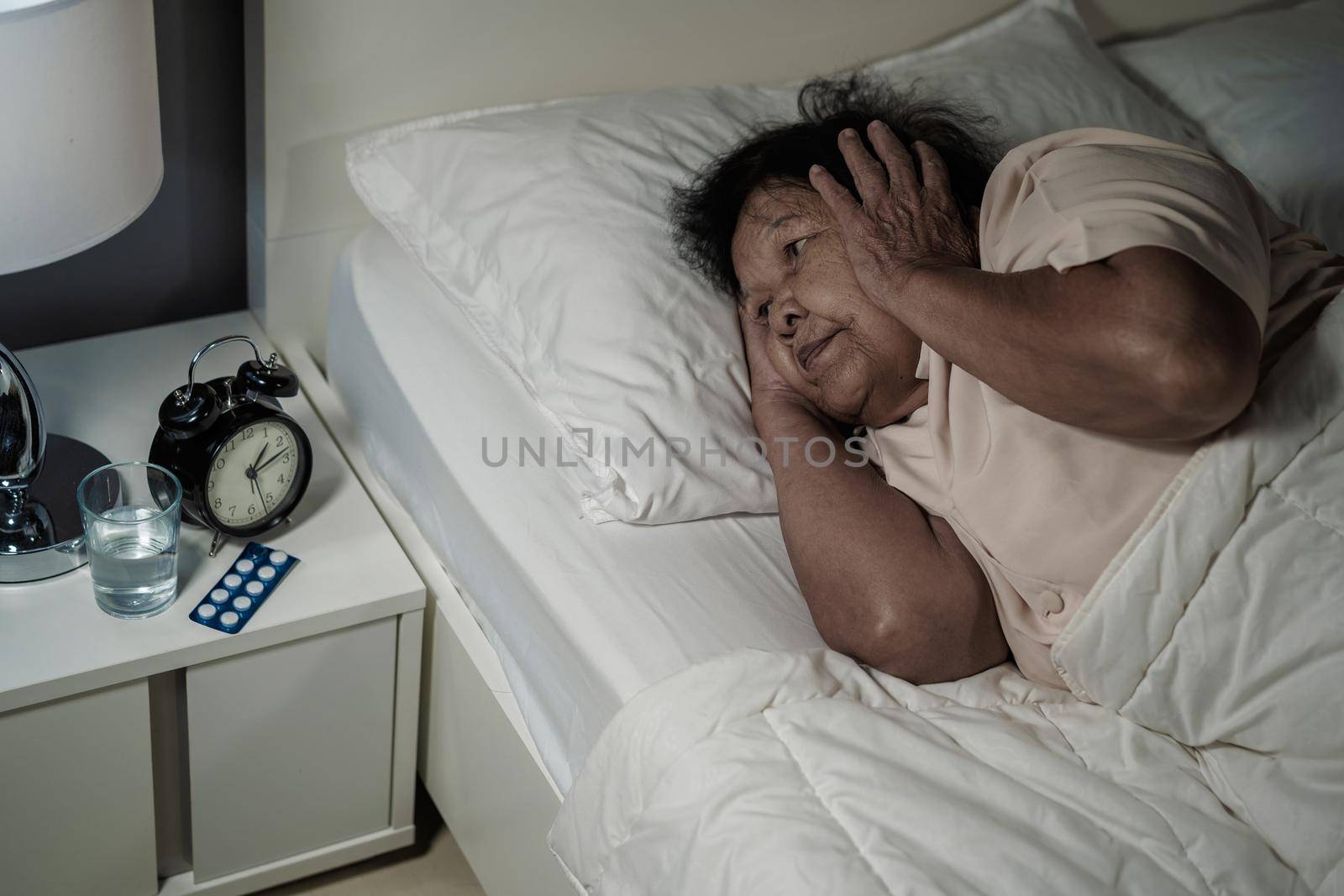 Old woman suffering from insomnia is trying to sleep in bed at night