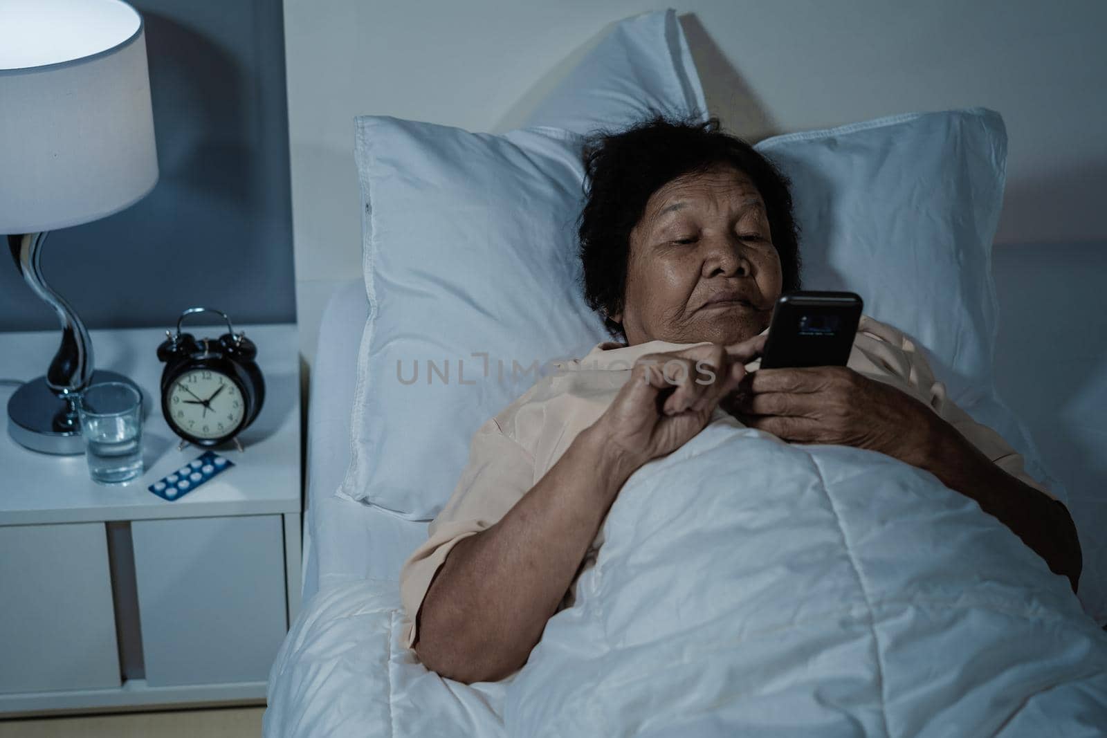 senior woman using mobile phone on a bed at night