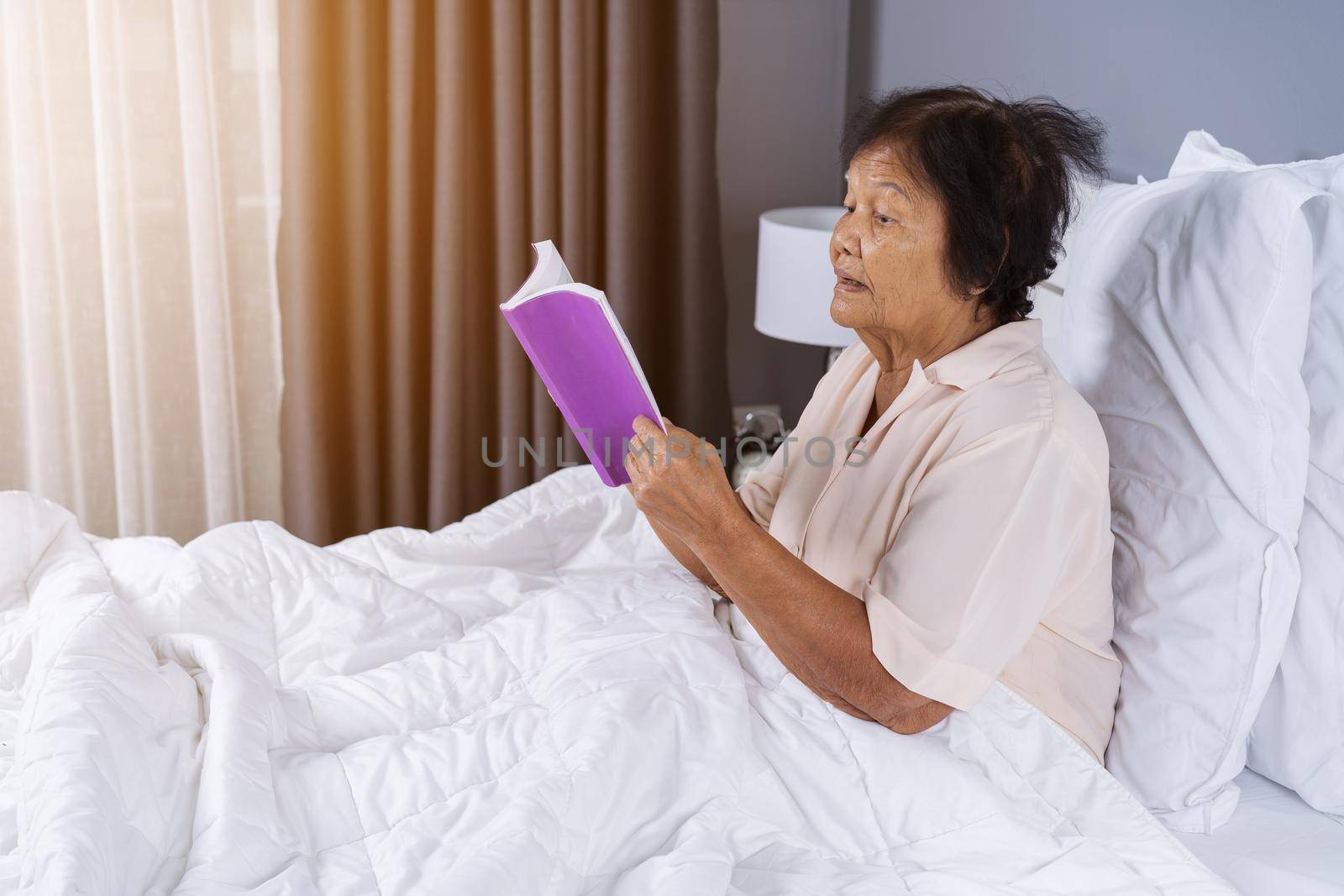 old woman reading a book on bed in bedroom