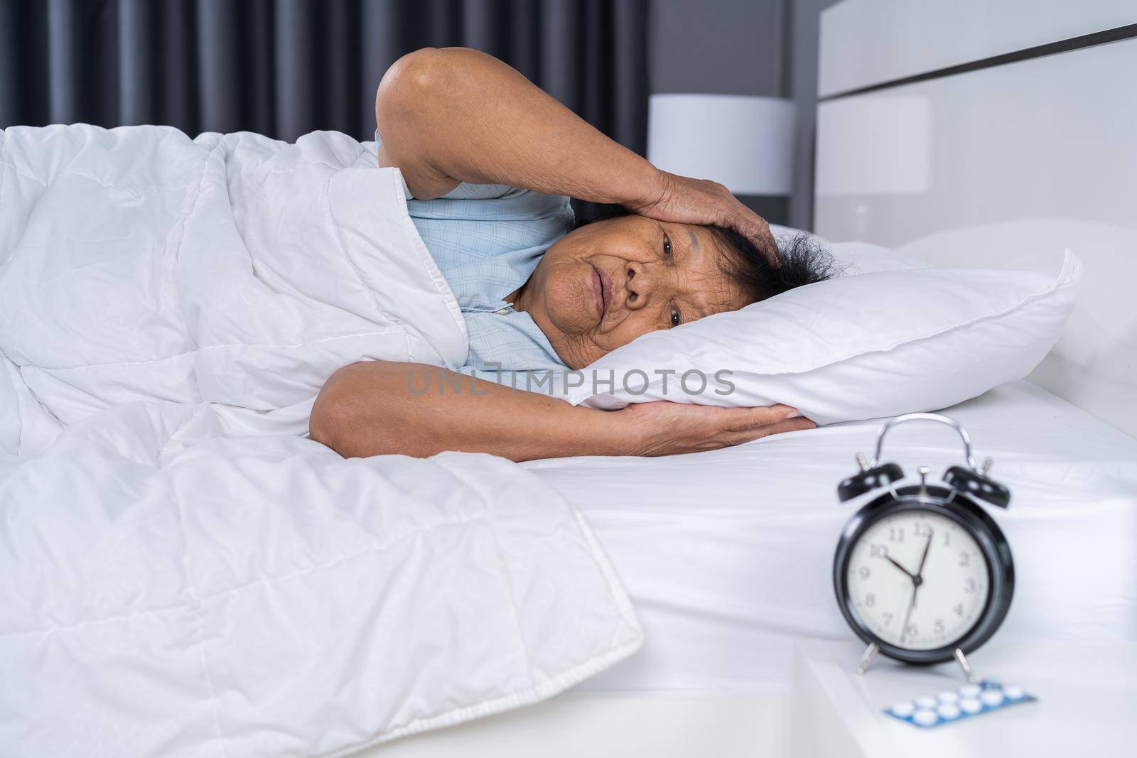 Old woman suffering from insomnia is trying to sleep in bed at night