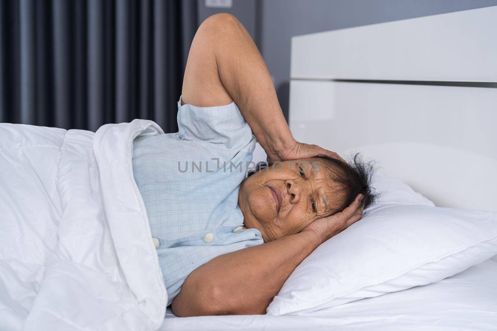 Old woman suffering from insomnia is trying to sleep in a bed