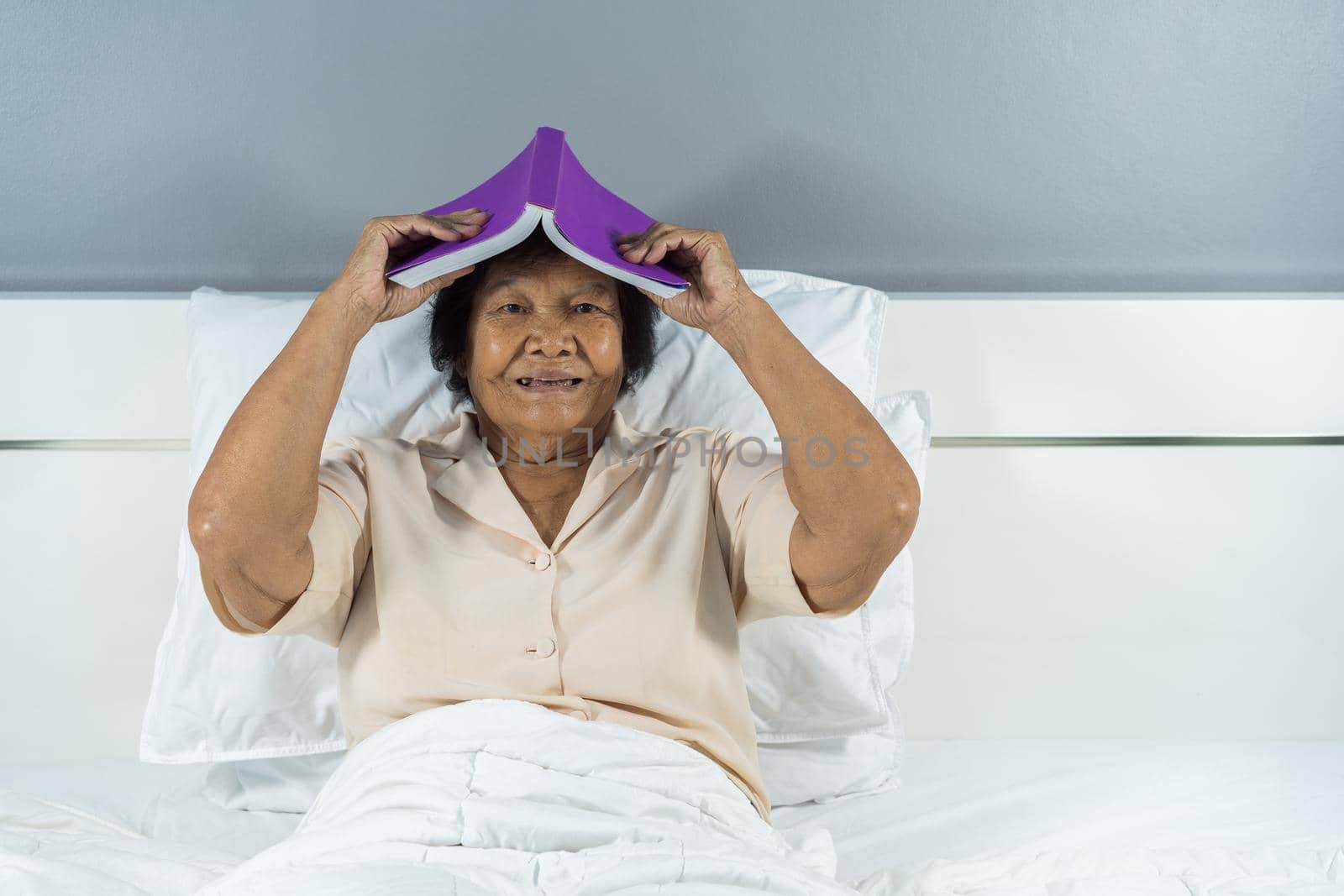 happy old woman in bed holding a book on her head