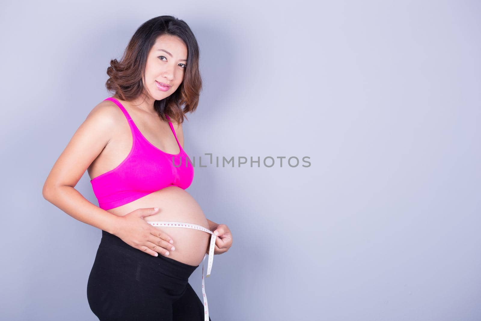 beautiful Pregnant woman with measuring tape on gray background