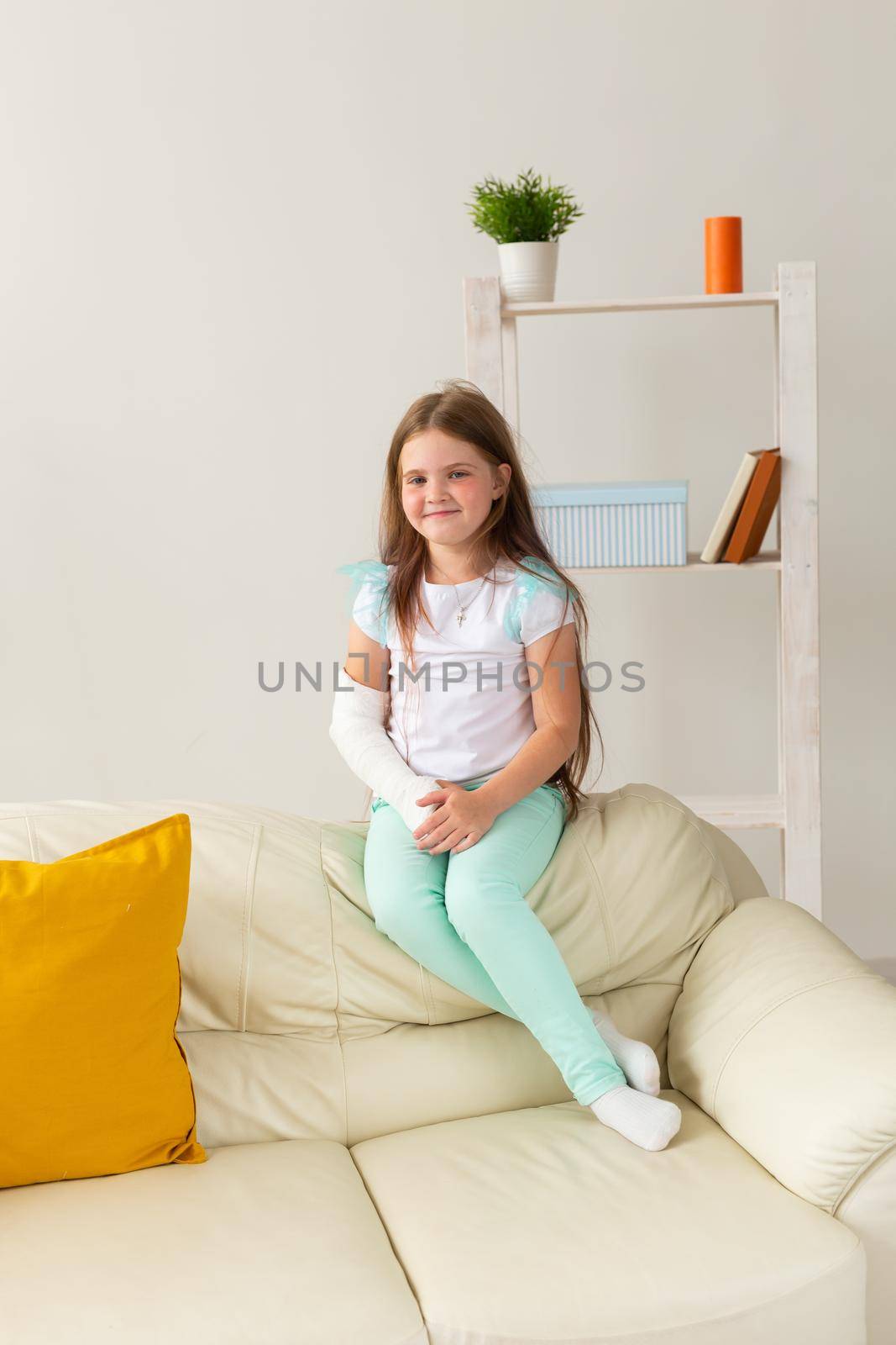 Child with a cast on a broken wrist or arm smiling and having fun on a couch. Positive attitude, recovery and kid.