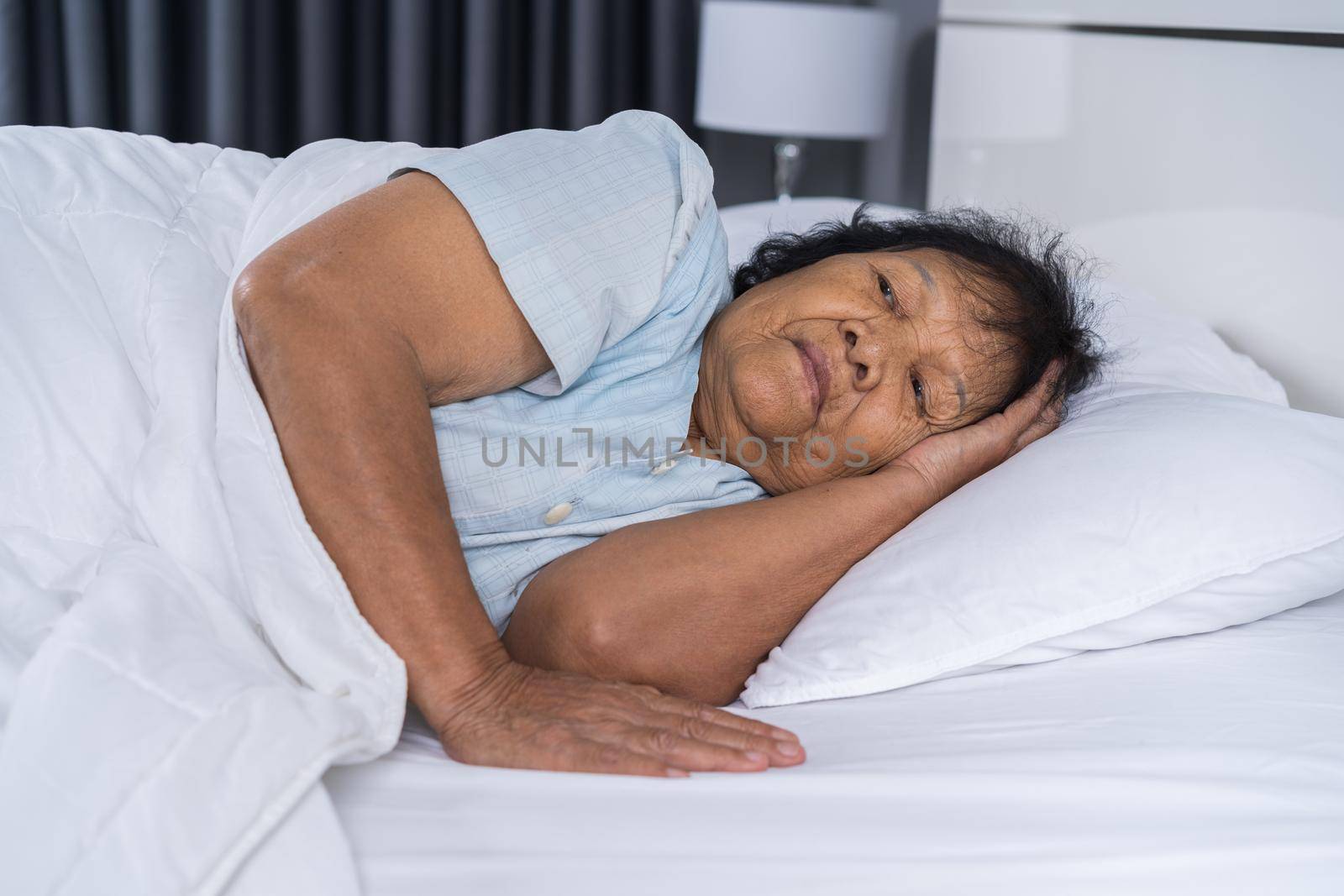 Old woman suffering from insomnia is trying to sleep in a bed