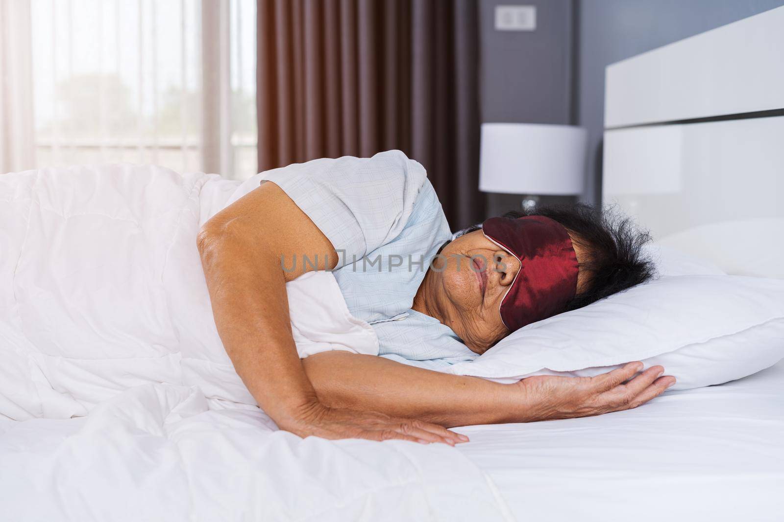 senior woman with eye mask sleeping on a bed in bedroom