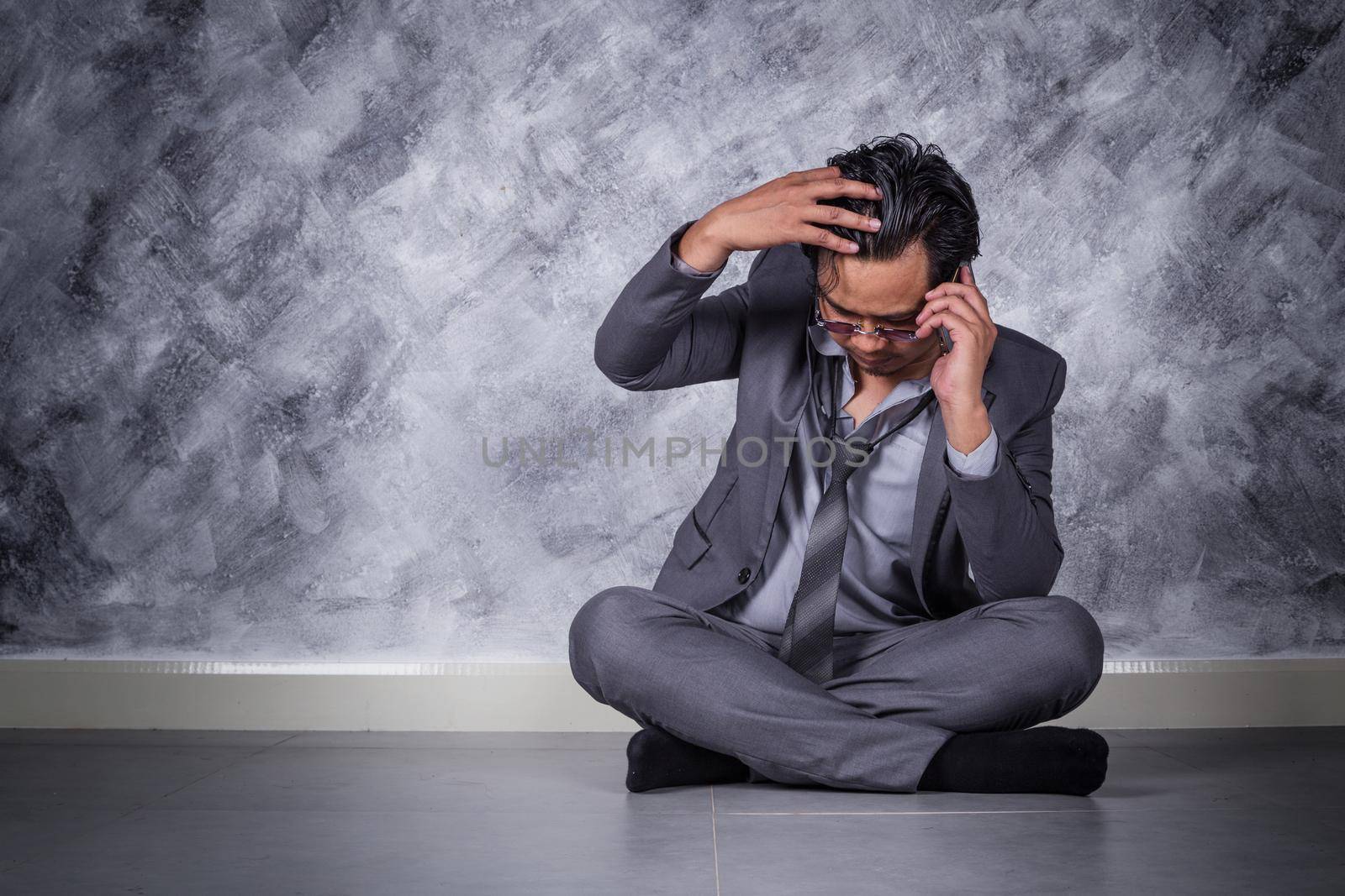 young depressed businessman with mobile phone and sitting on the floor 