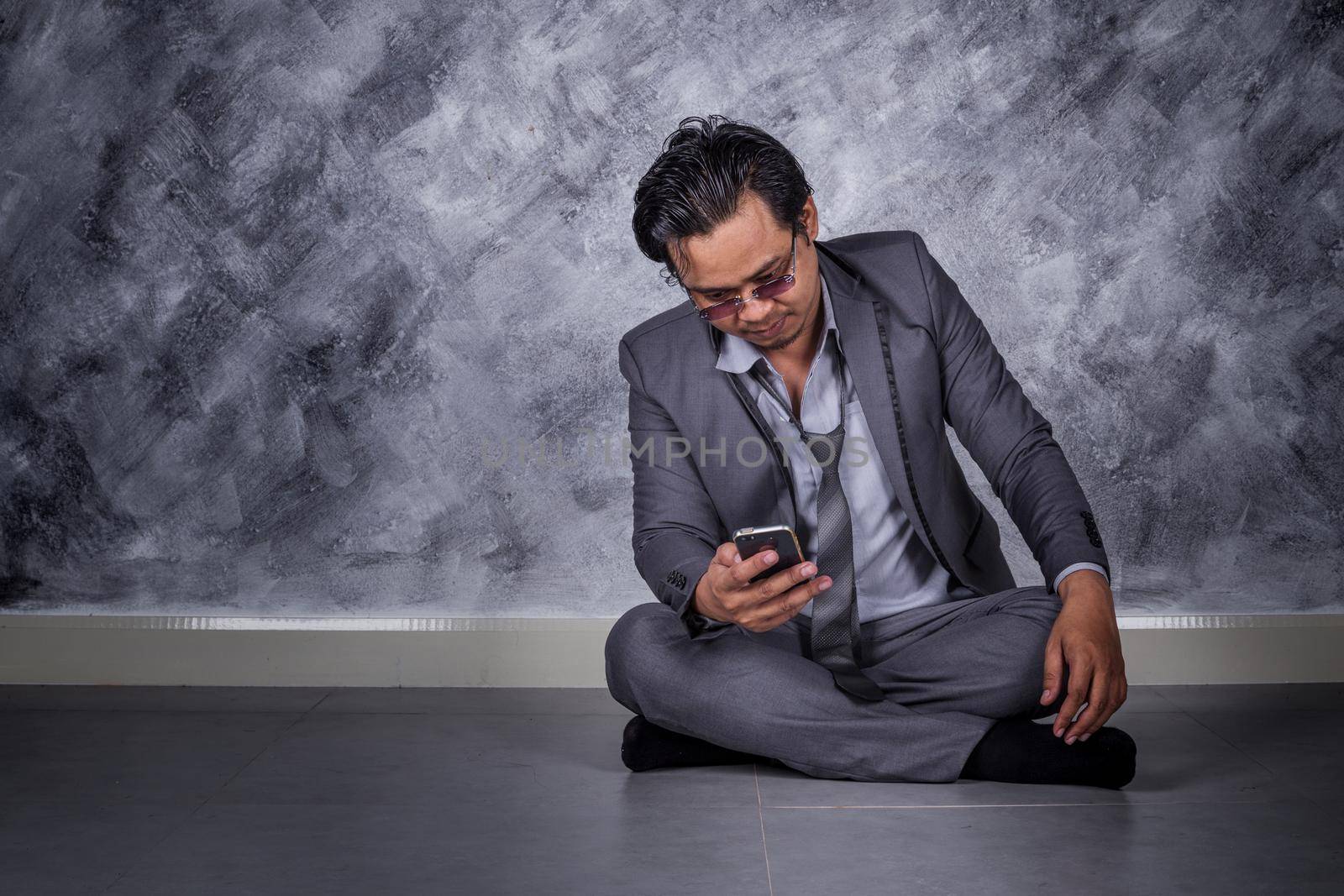 young depressed businessman with mobile phone and sitting on the floor 