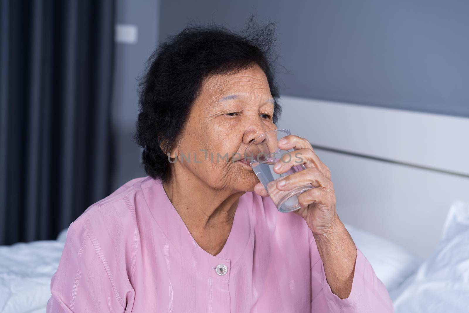 Senior woman drinking water in the bedroom