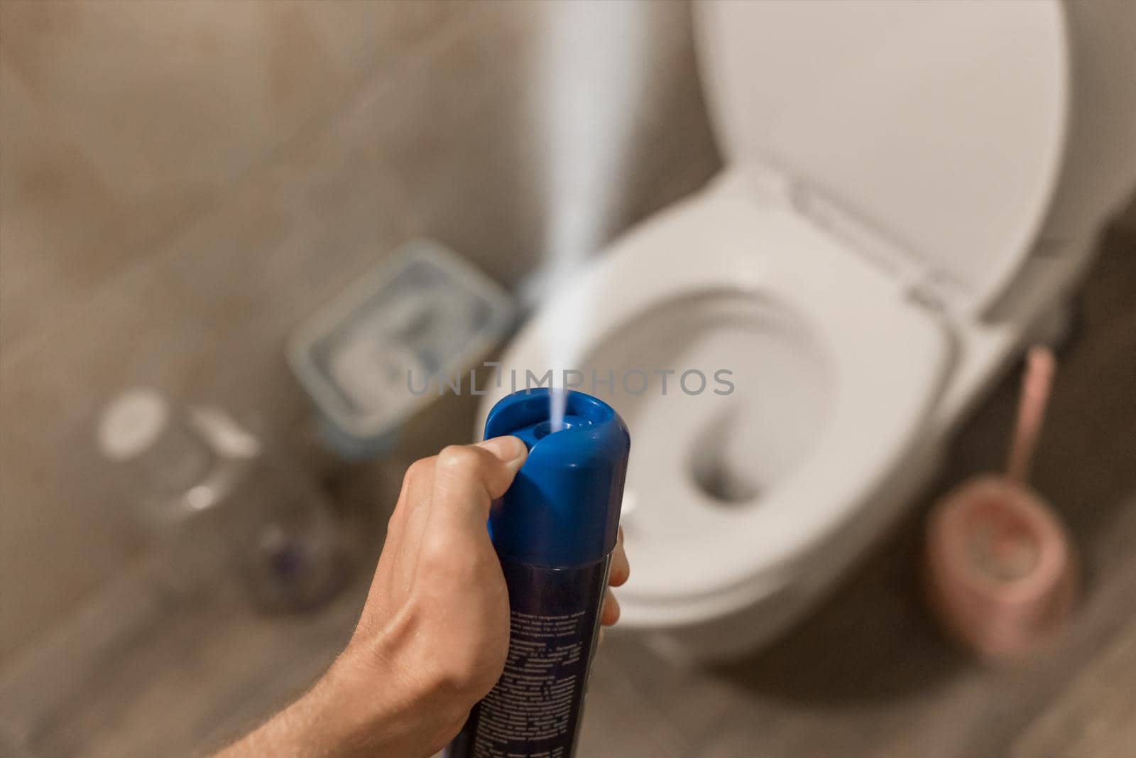 The guy's hand holds and sprays the air freshener in the toilet or bathroom. Home Hygiene Concept.