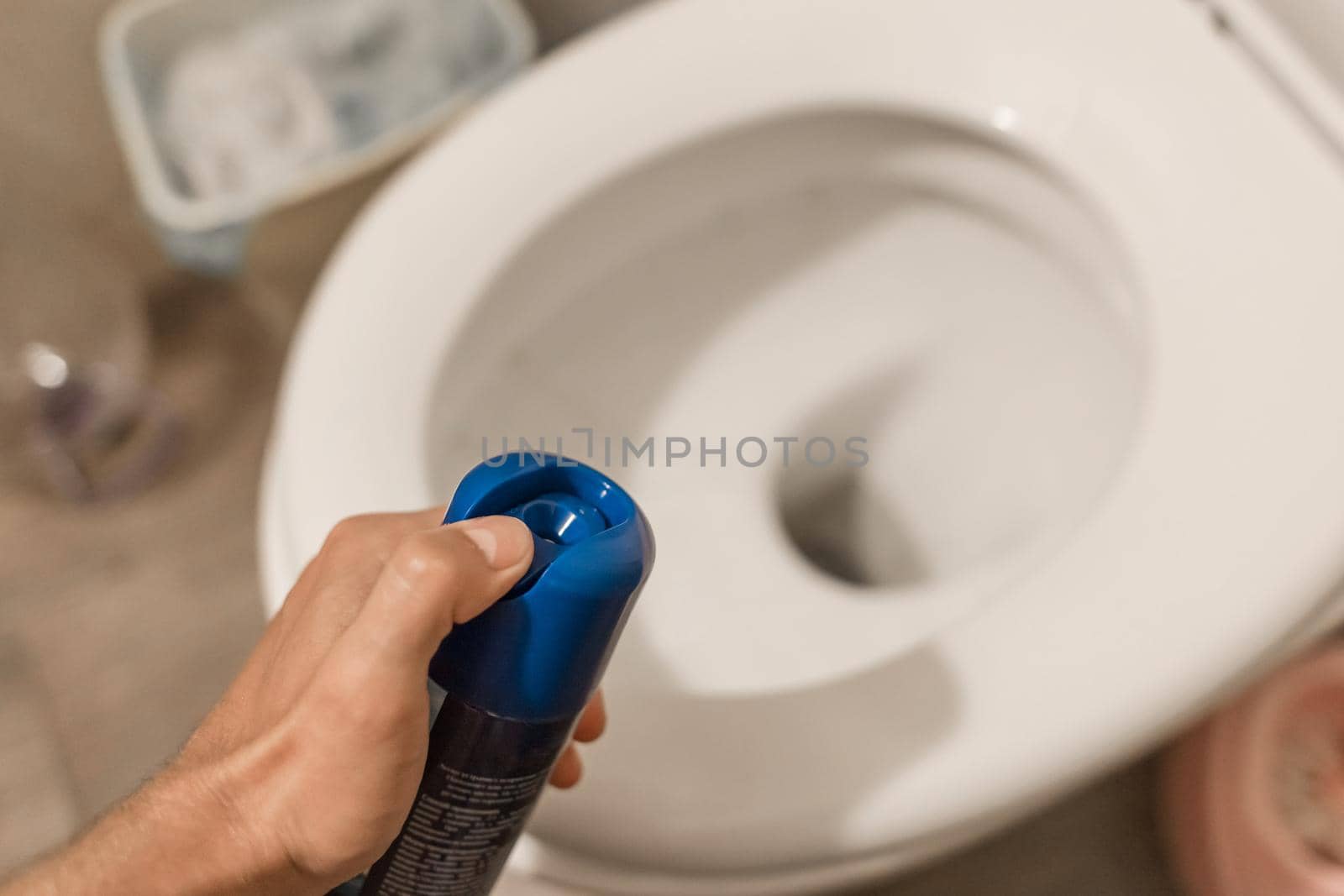 The guy's hand holds and sprays the air freshener in the toilet or bathroom. Home Hygiene Concept.