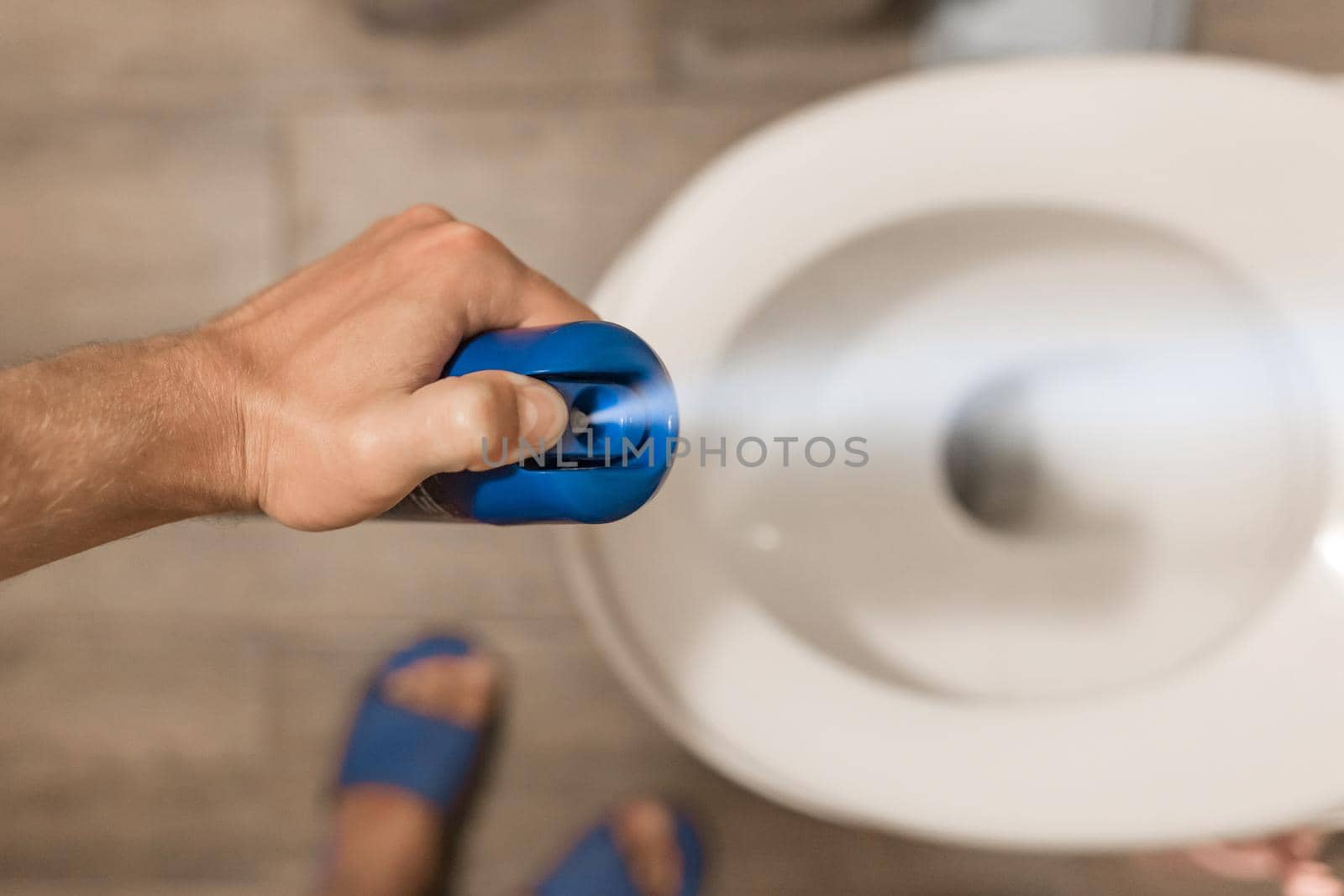The guy's hand holds and sprays the air freshener in the toilet or bathroom. Home Hygiene Concept.
