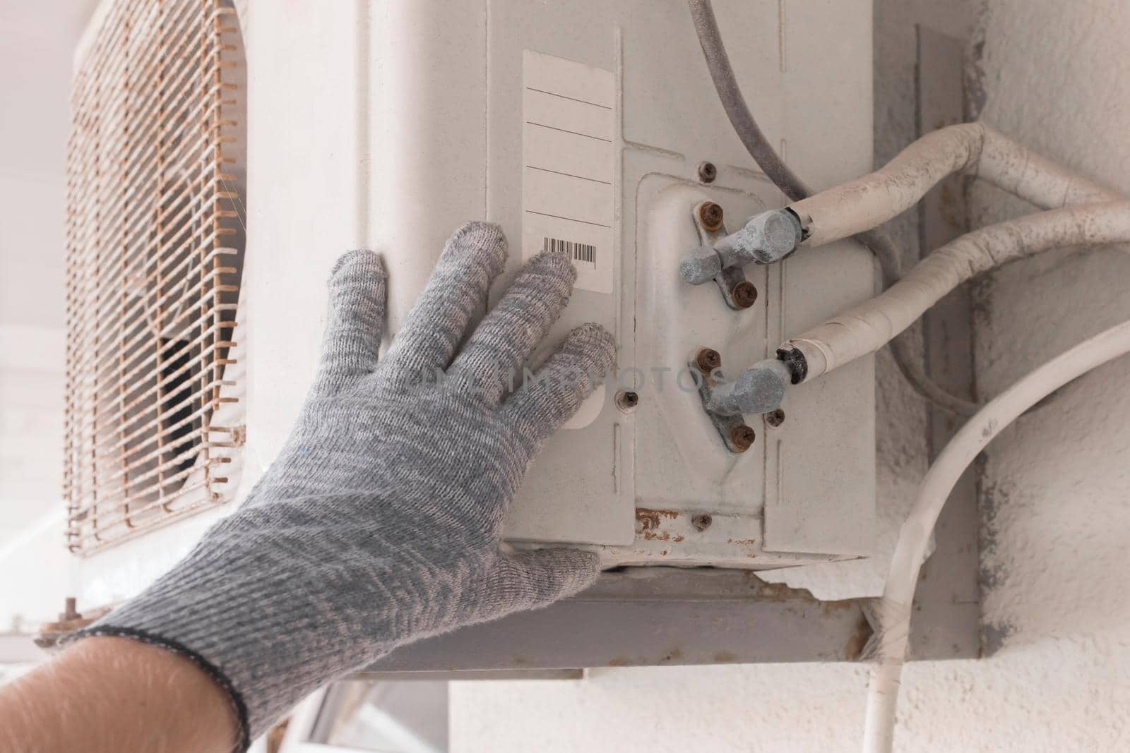 The hand of an air conditioner repair and maintenance specialist in a construction glove working with air-conditioned old equipment by AYDO8