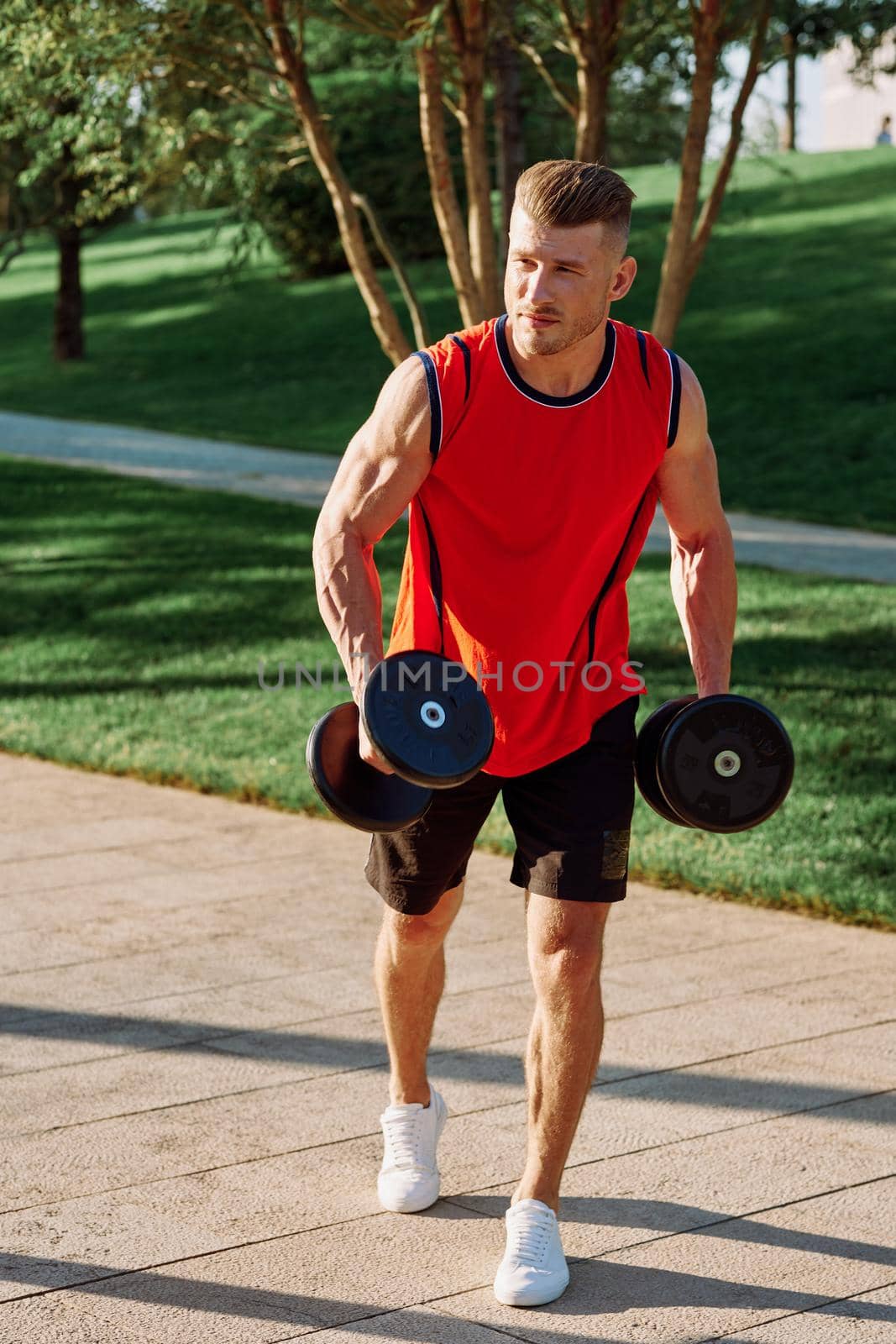 athletic man with dumbbells in his hands outdoors in the park. High quality photo