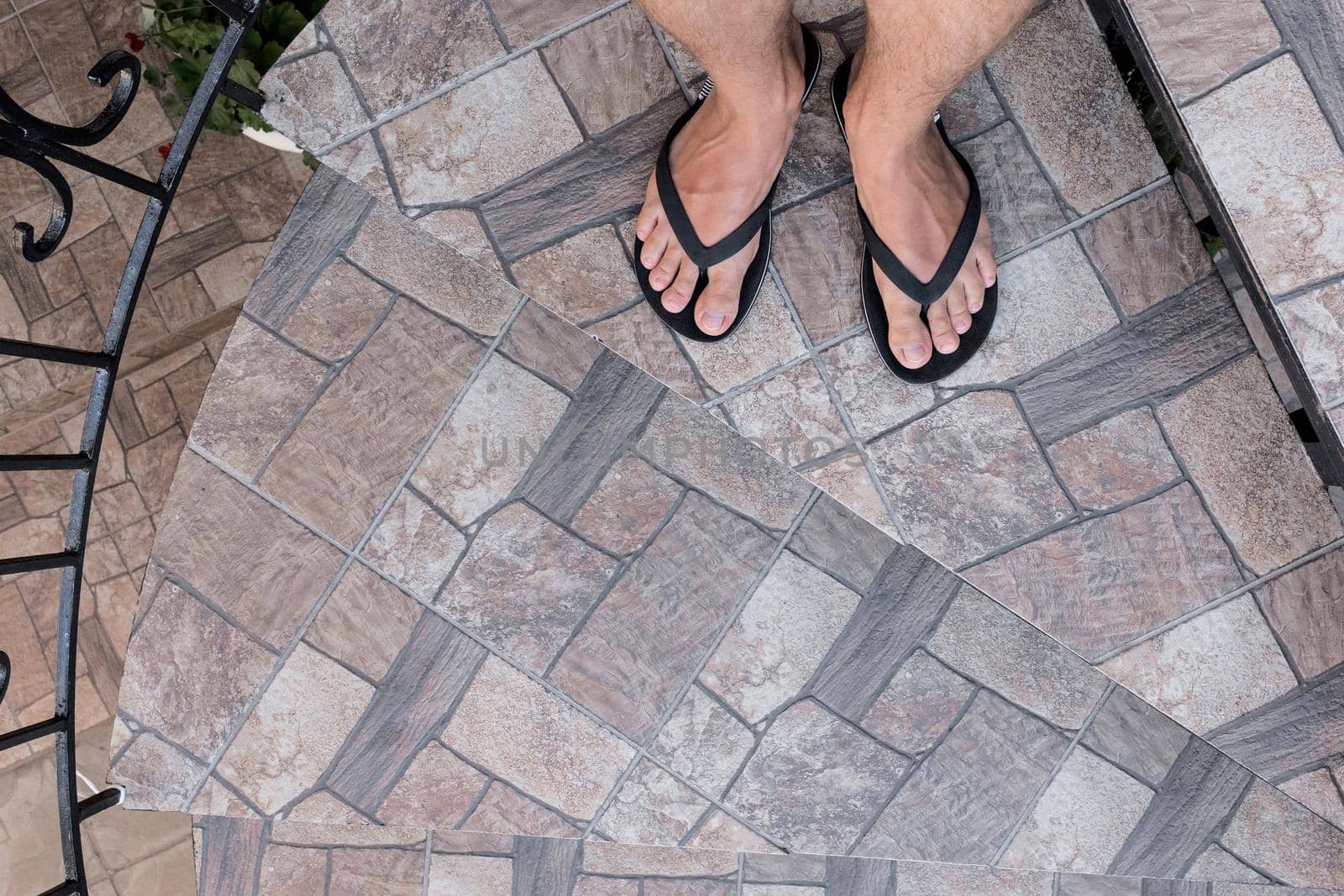 Men's legs in black flip flops stands on the stairs and go down. Walking style.