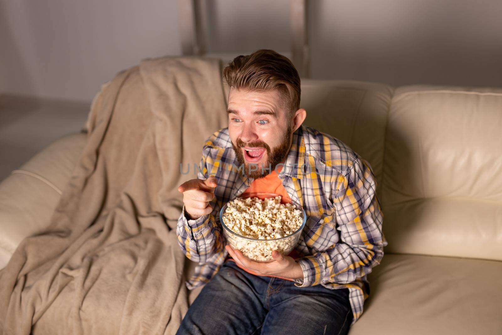 Bearded man watching film or sport games TV eating popcorn in house at night. Cinema, championship and fan.